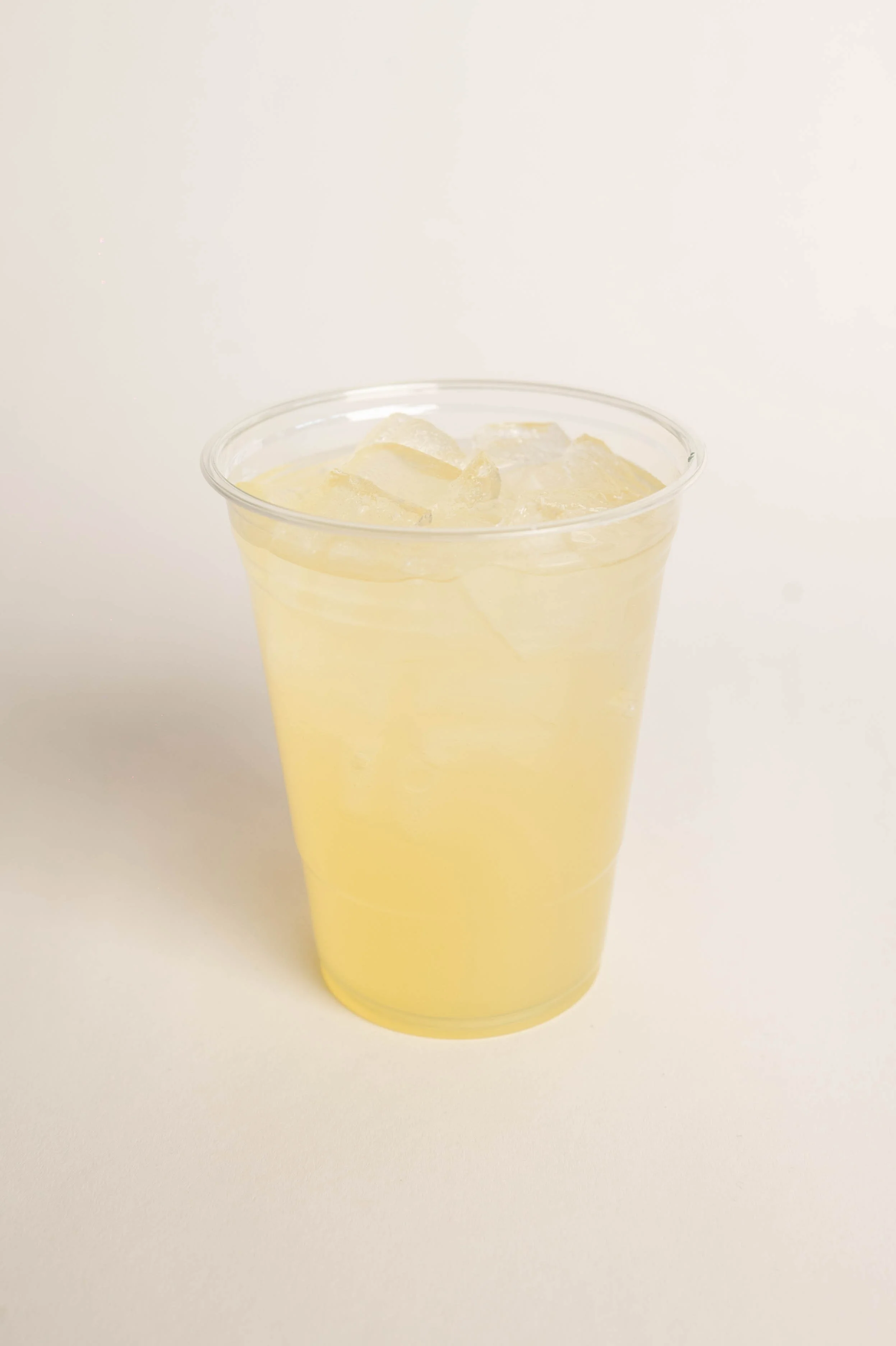 A clear plastic cup filled with pale yellow lemonade and ice cubes.