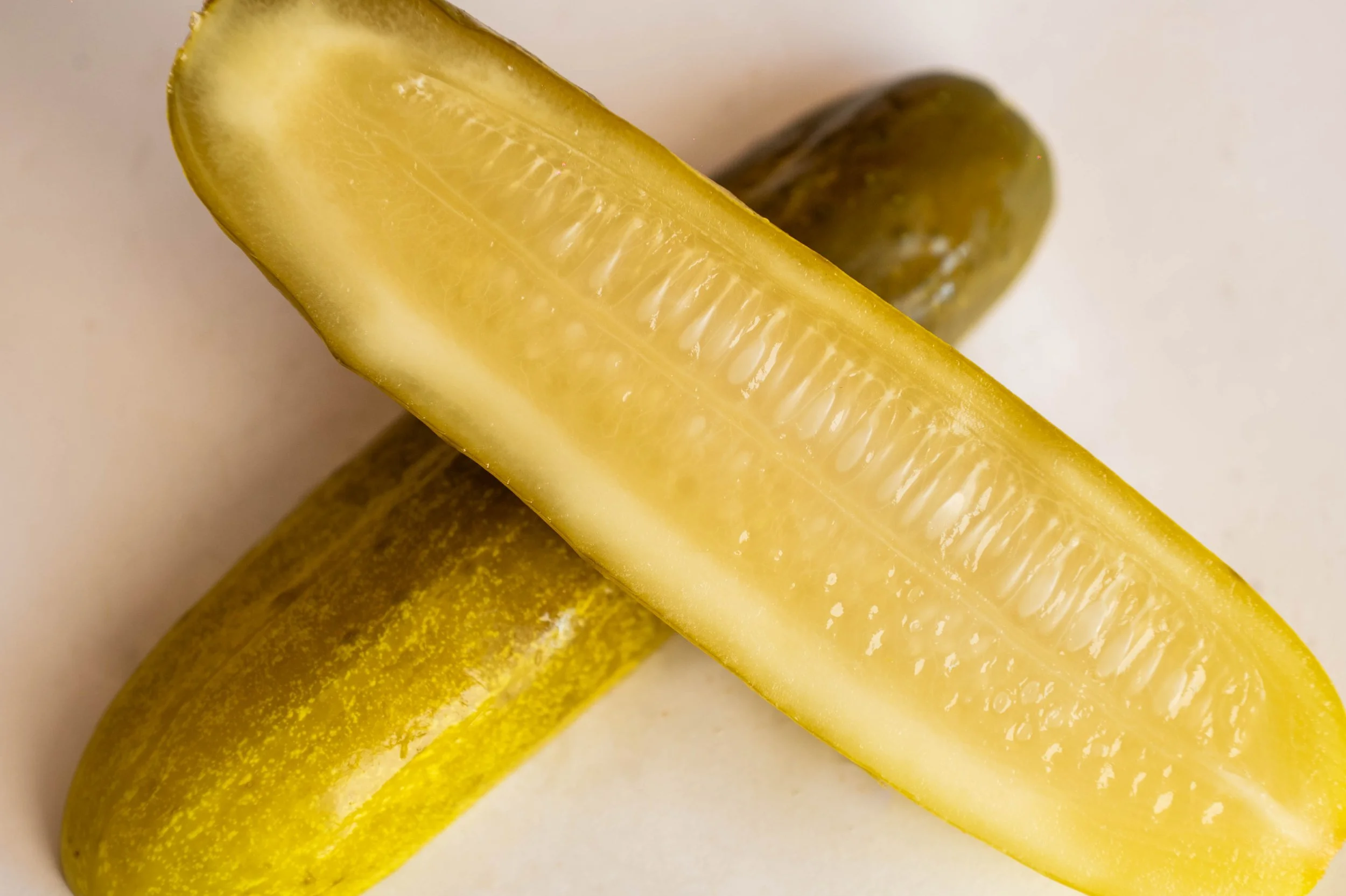 A close-up of a sliced yellow pickle with a bumpy green pickle in the background.
