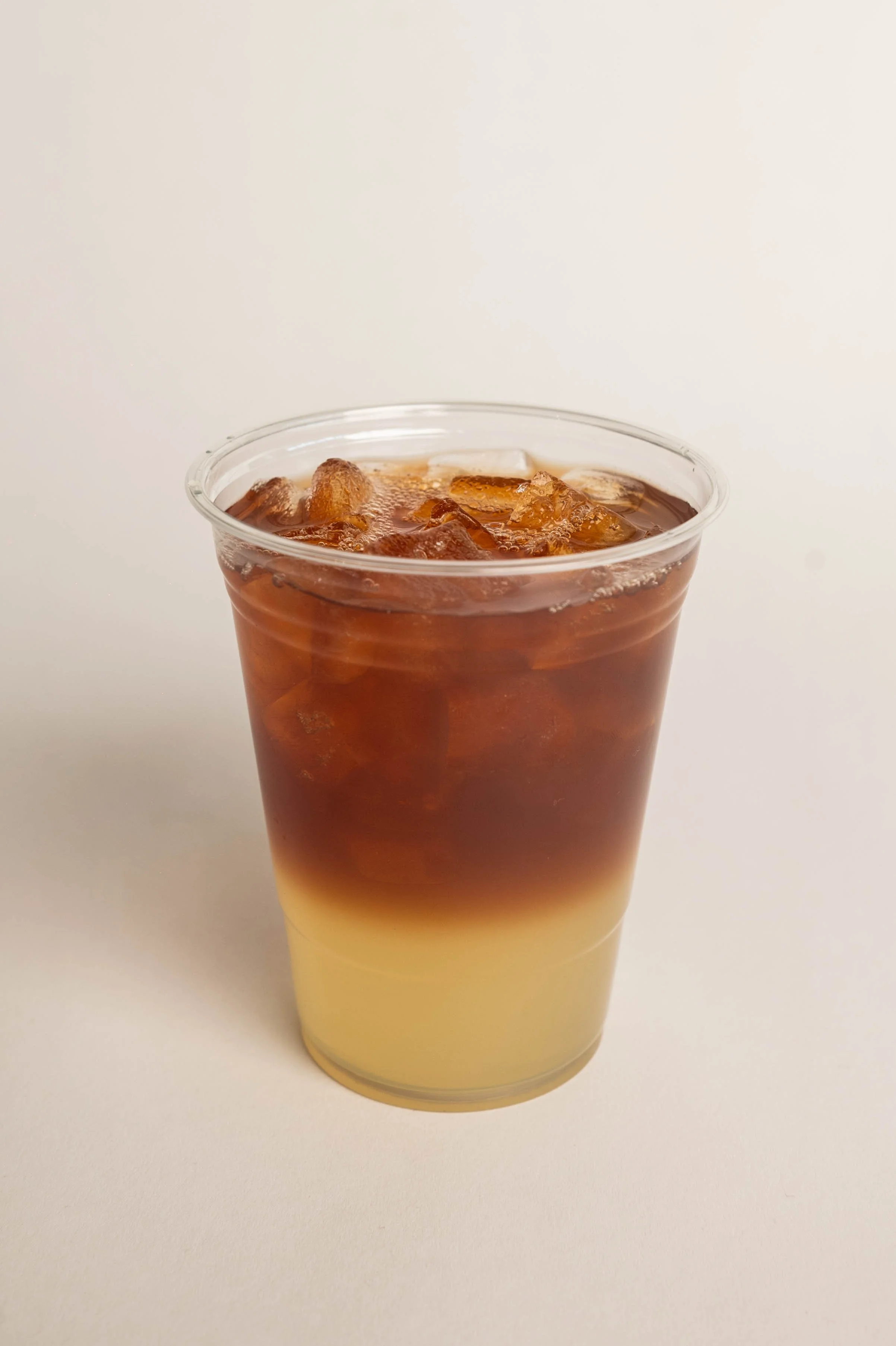 A clear plastic cup filled with iced coffee, showing a layered drink with cream at the bottom and coffee on top, against a plain white background.