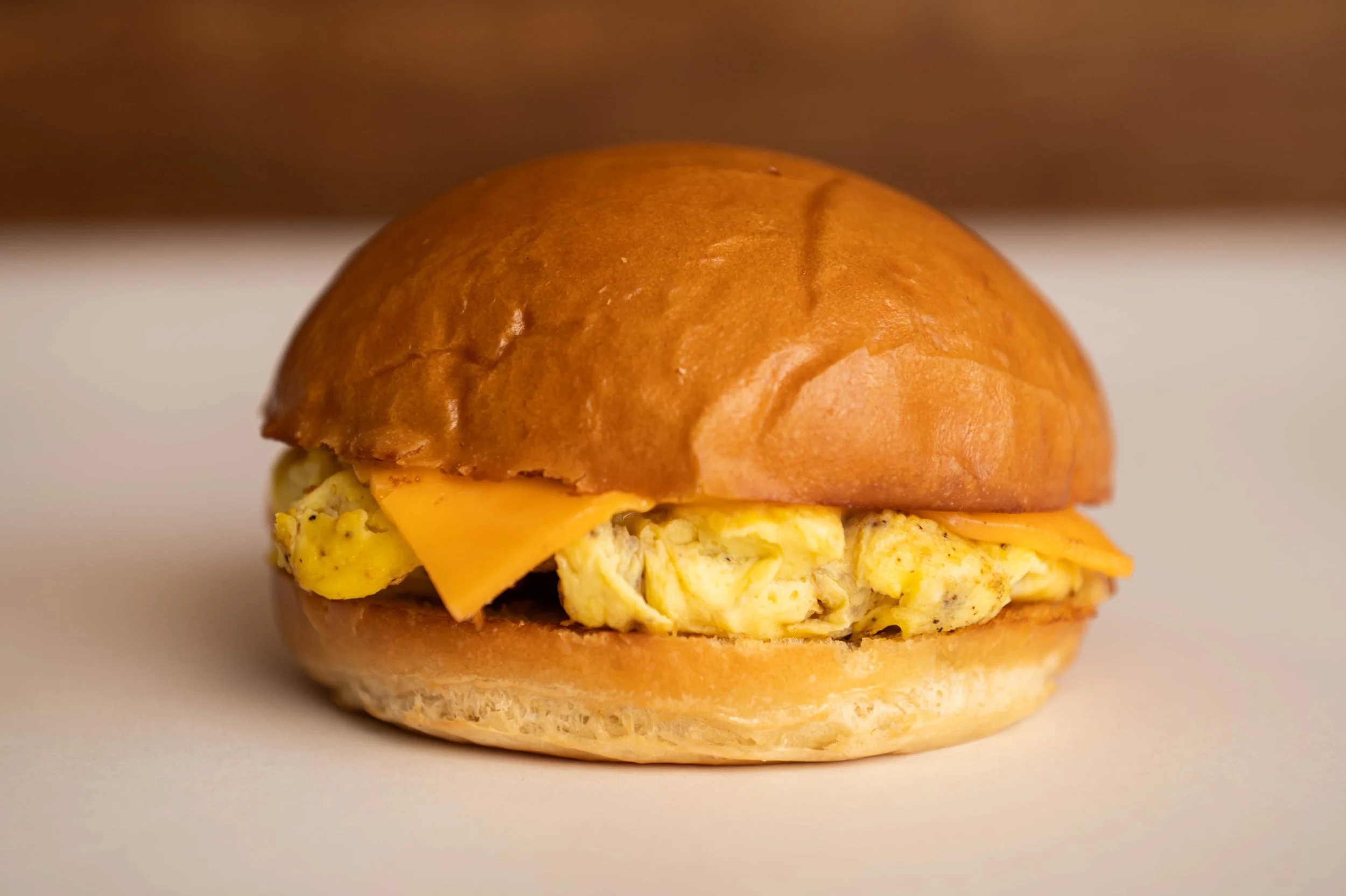 Close-up of a breakfast sandwich with scrambled eggs, cheddar cheese, and a toasted bun.
