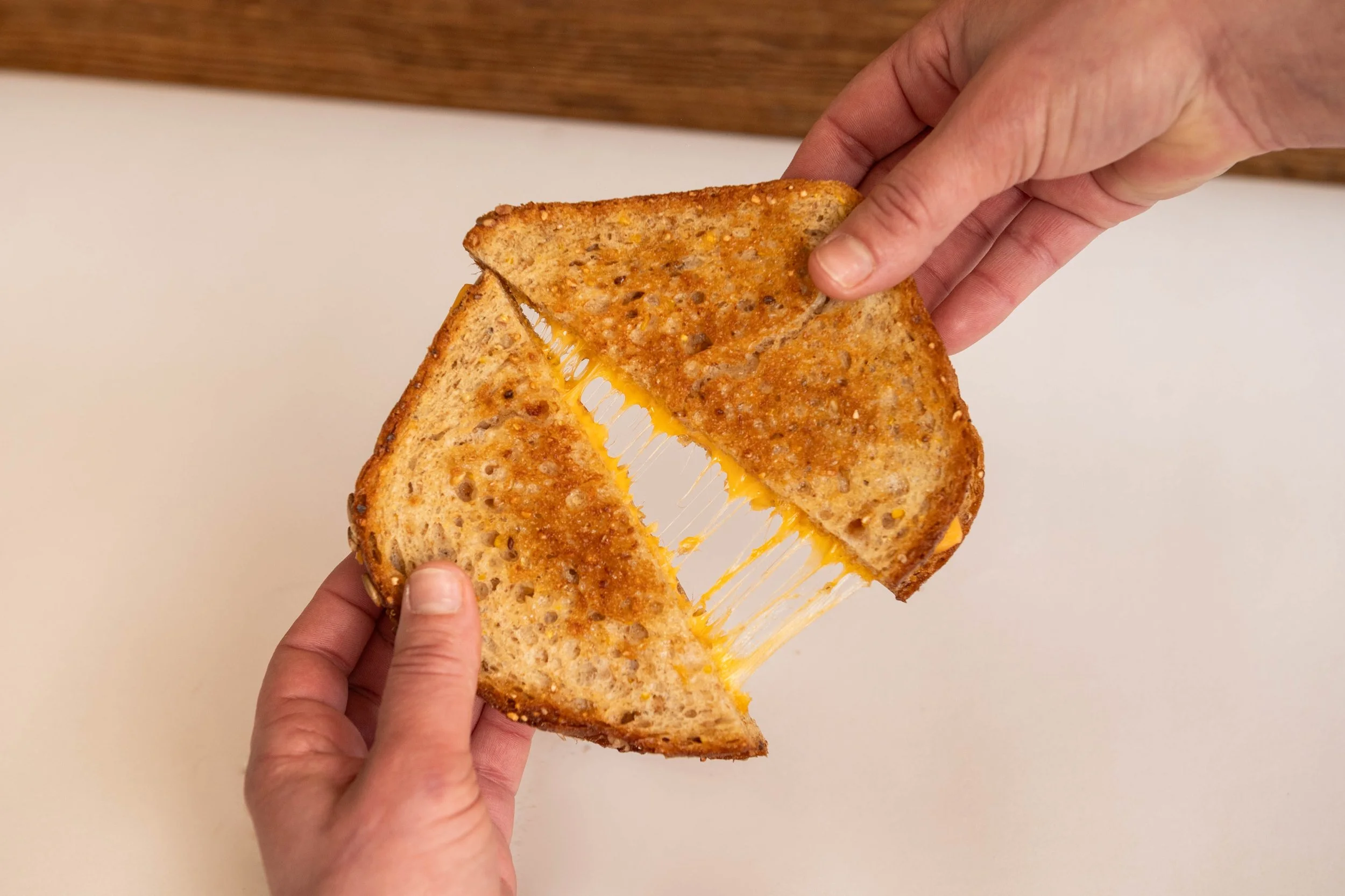 Two hands pulling apart a grilled cheese sandwich, stretching melted cheese.