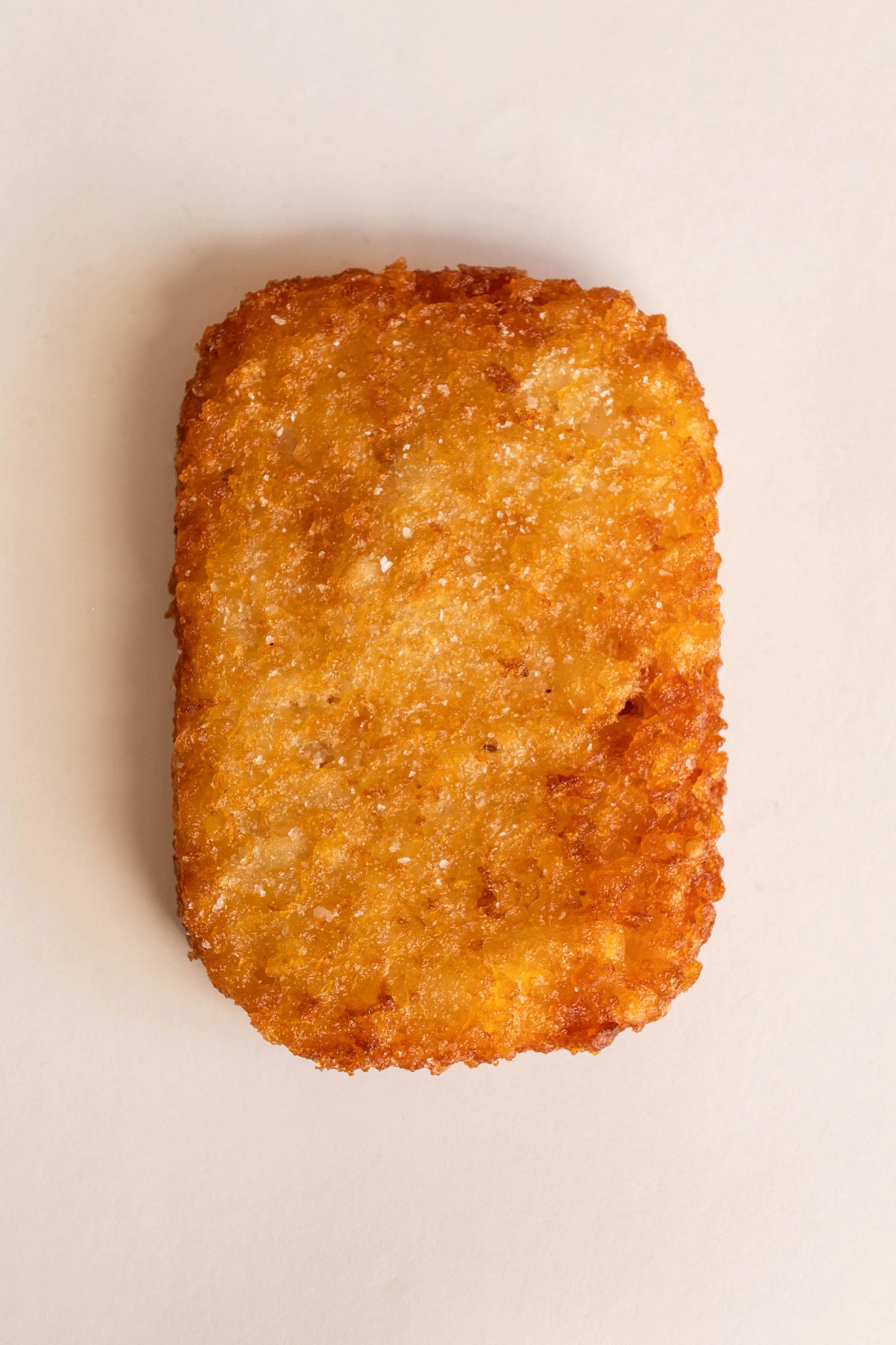 A close-up of a golden-brown, crispy breaded chicken nugget on a white background.