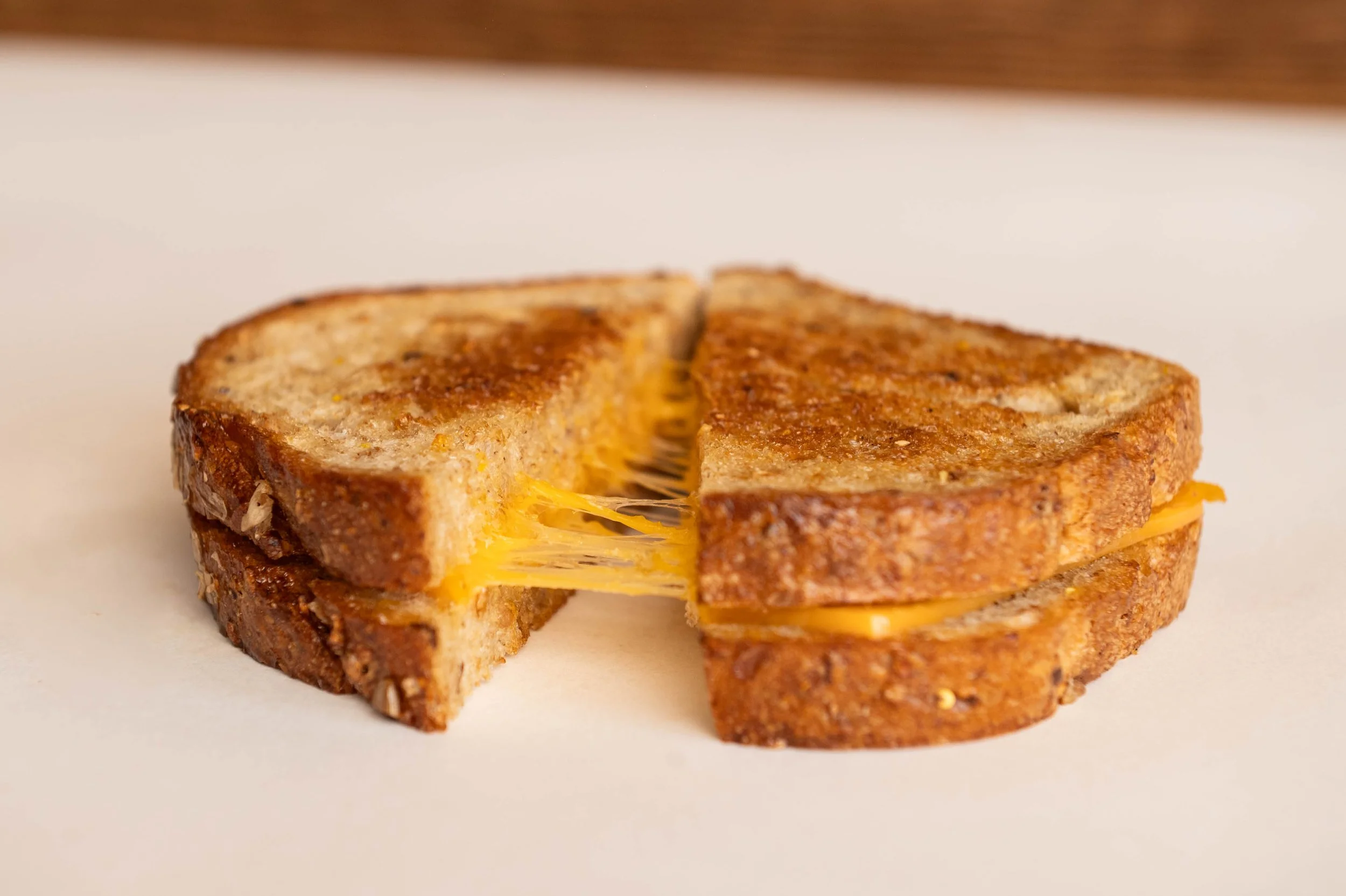 A grilled cheese sandwich cut in half, showing melted cheese inside, resting on a white surface with a blurred background.