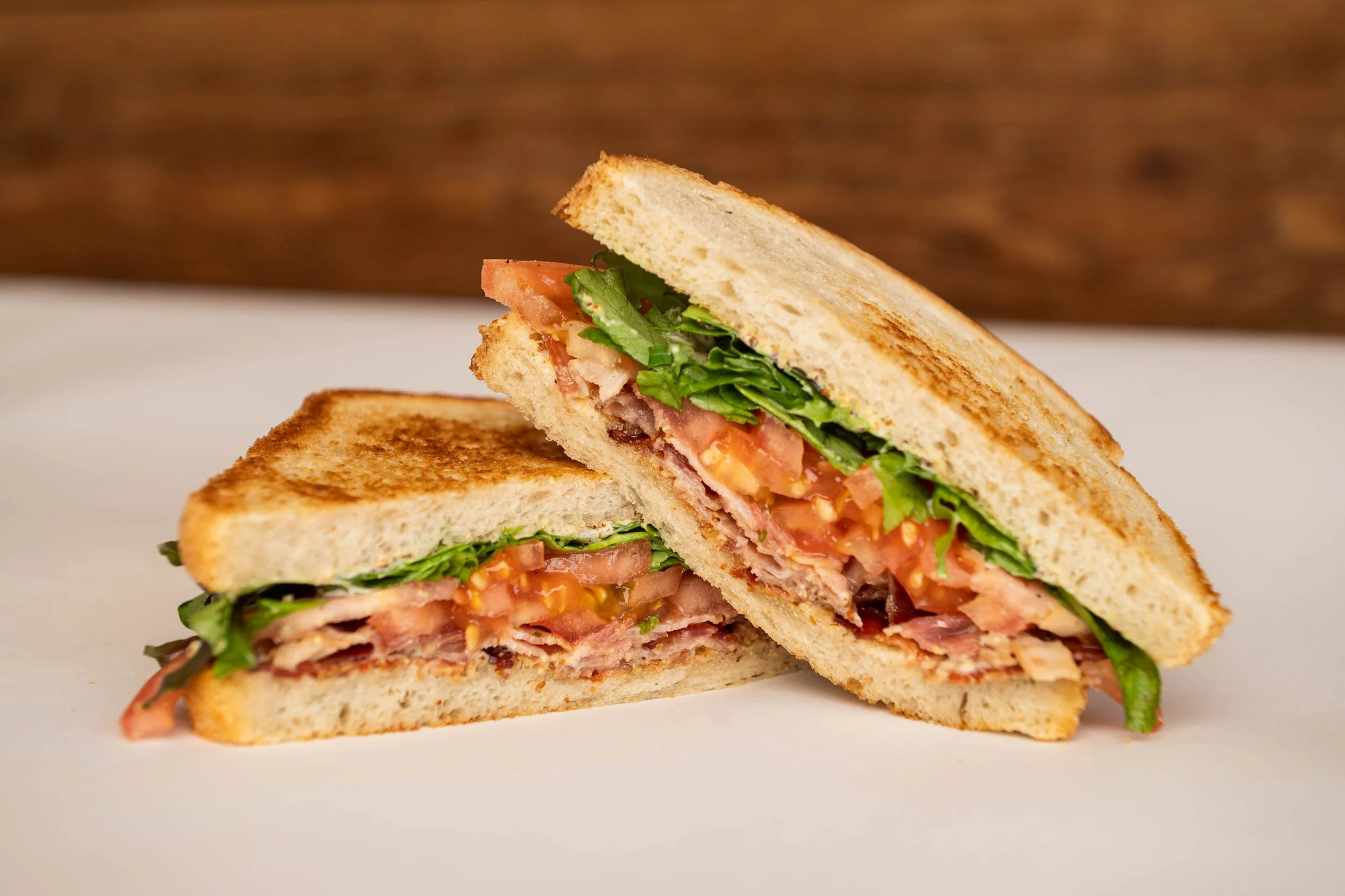 Close-up of a toasted sandwich cut in half, showing layers of bacon, lettuce, tomato, and cheese.