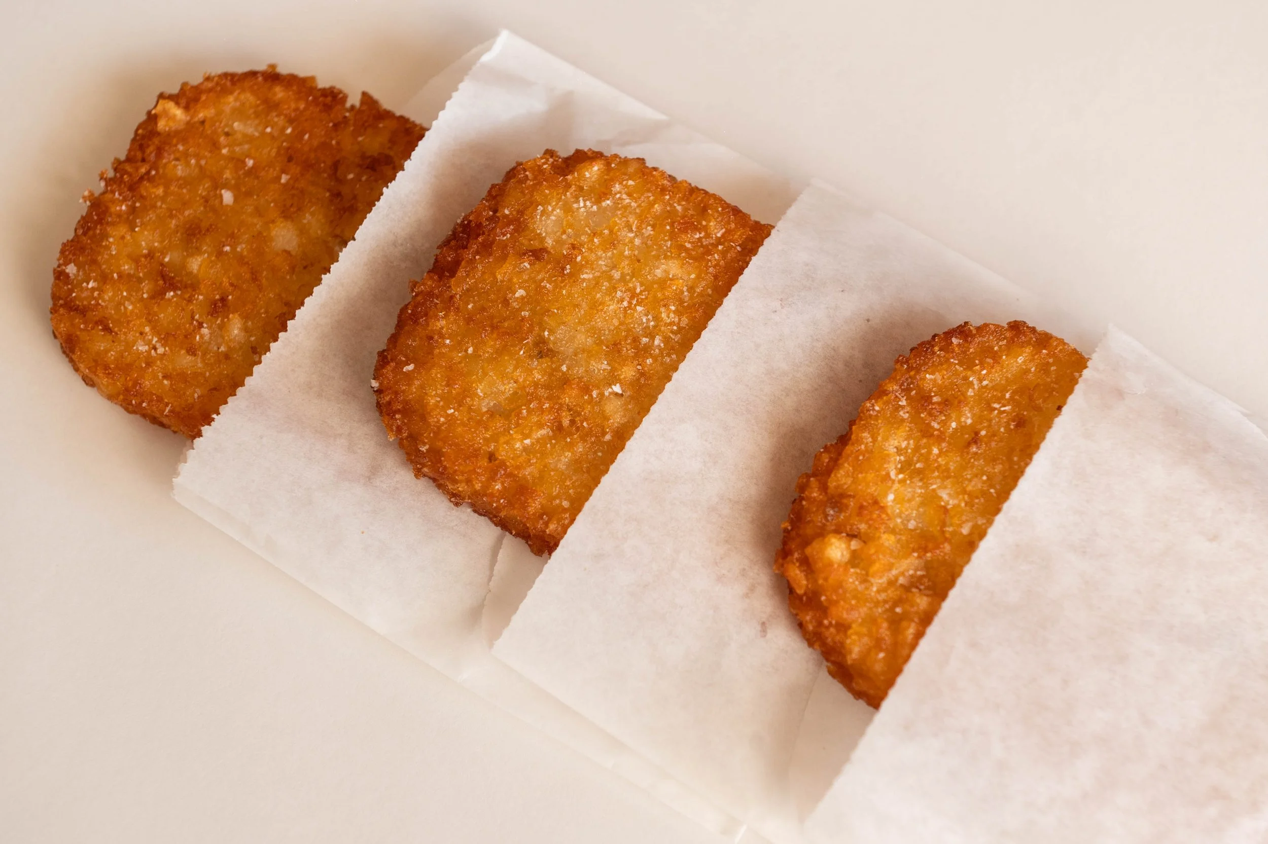 Three pieces of fried food, likely fish filets, on white parchment paper, on a white background.