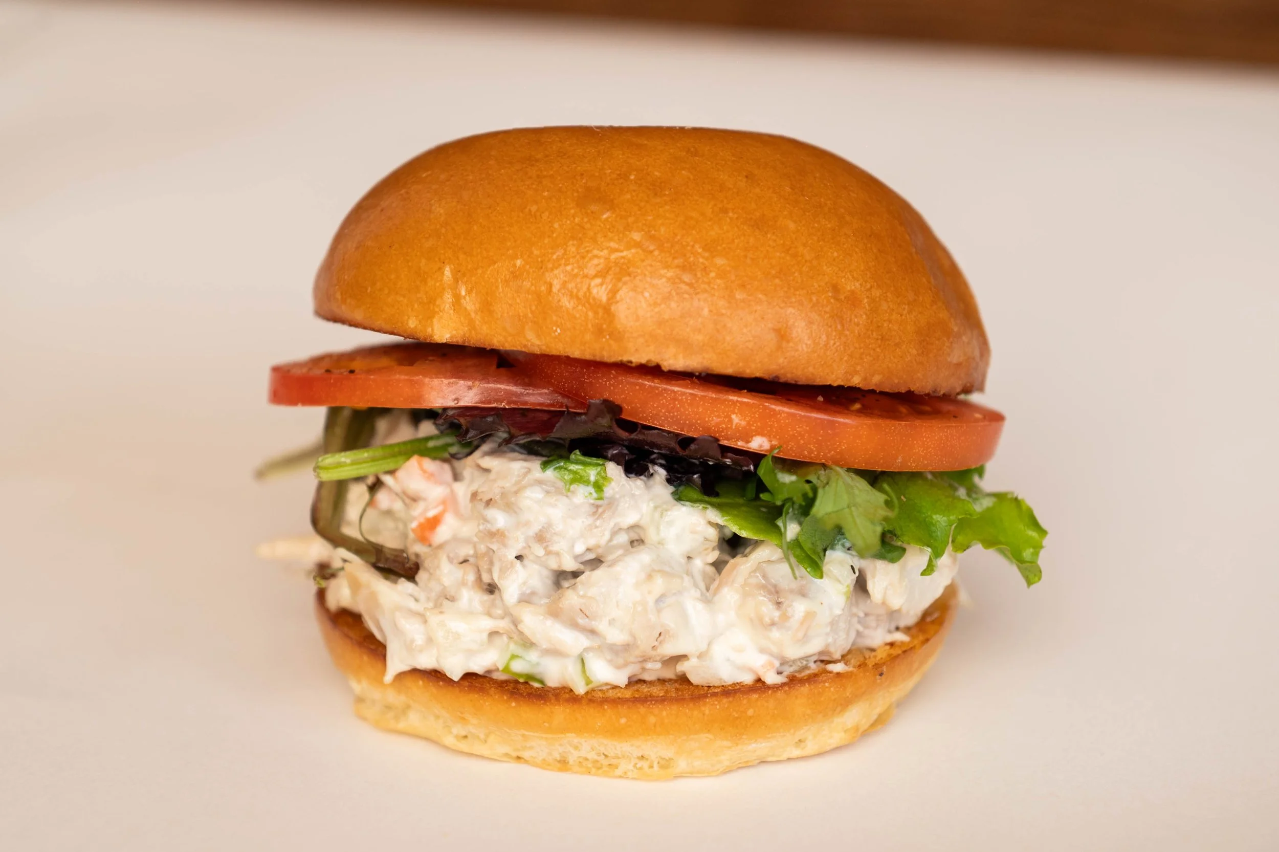 Close-up of a chicken salad sandwich with lettuce, tomato, and bread bun on a white surface.