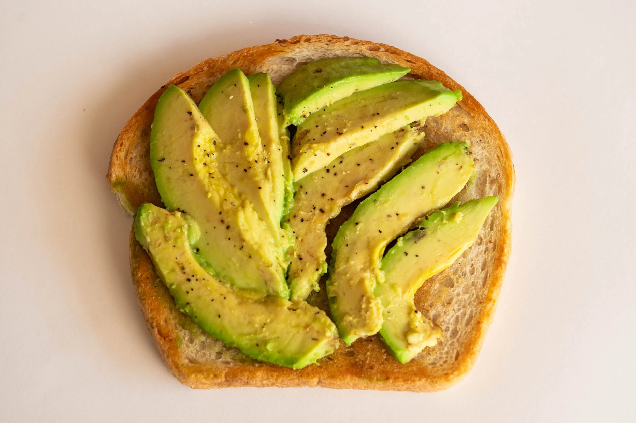 Slice of toasted bread topped with sliced avocado and sprinkled with black pepper.