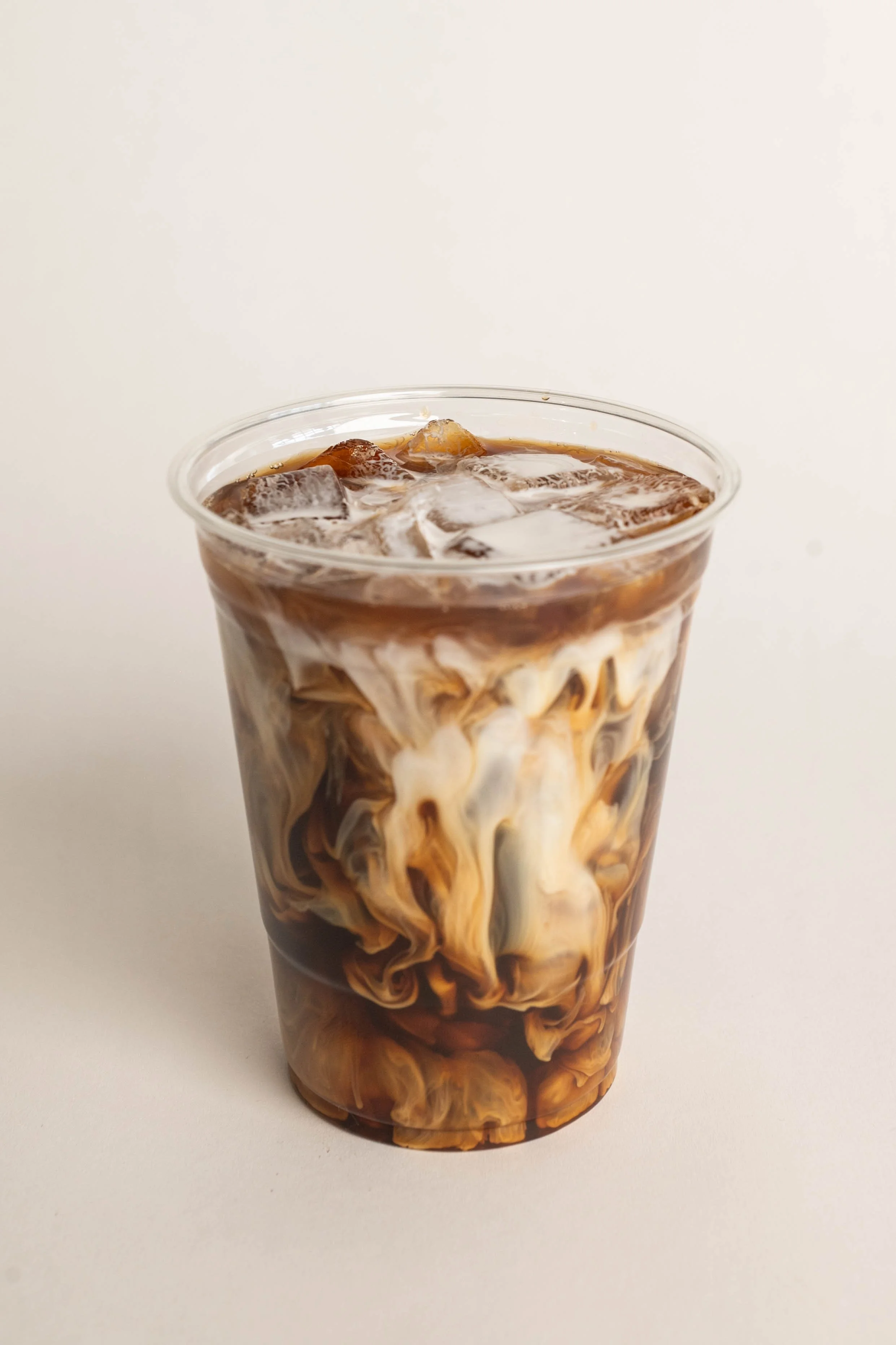 A clear plastic cup filled with iced coffee and cream swirling together.