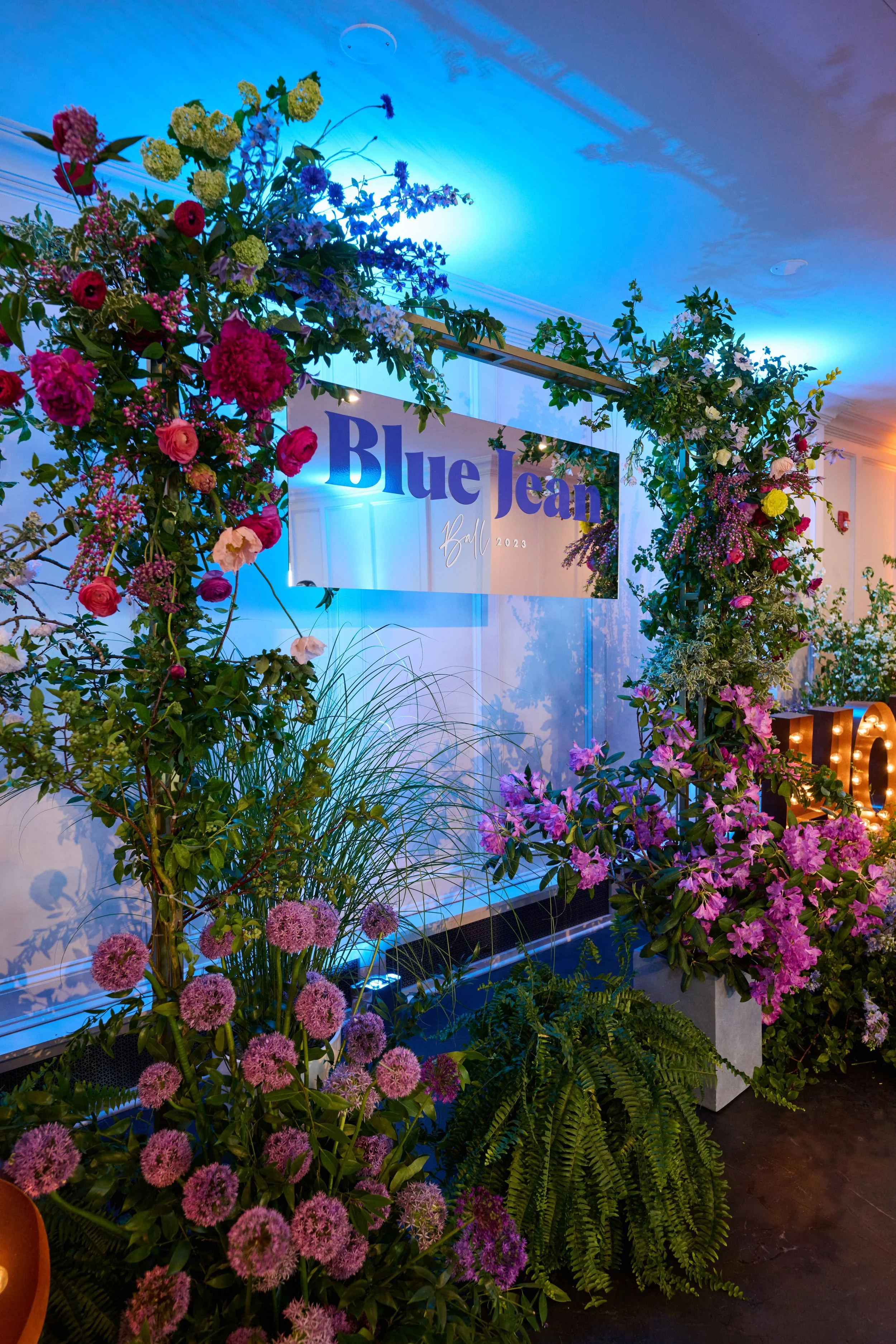 Decorative flower arch with pink, purple, yellow, and white flowers over a sign that reads 'Blue Jean Ball 2023' at an event