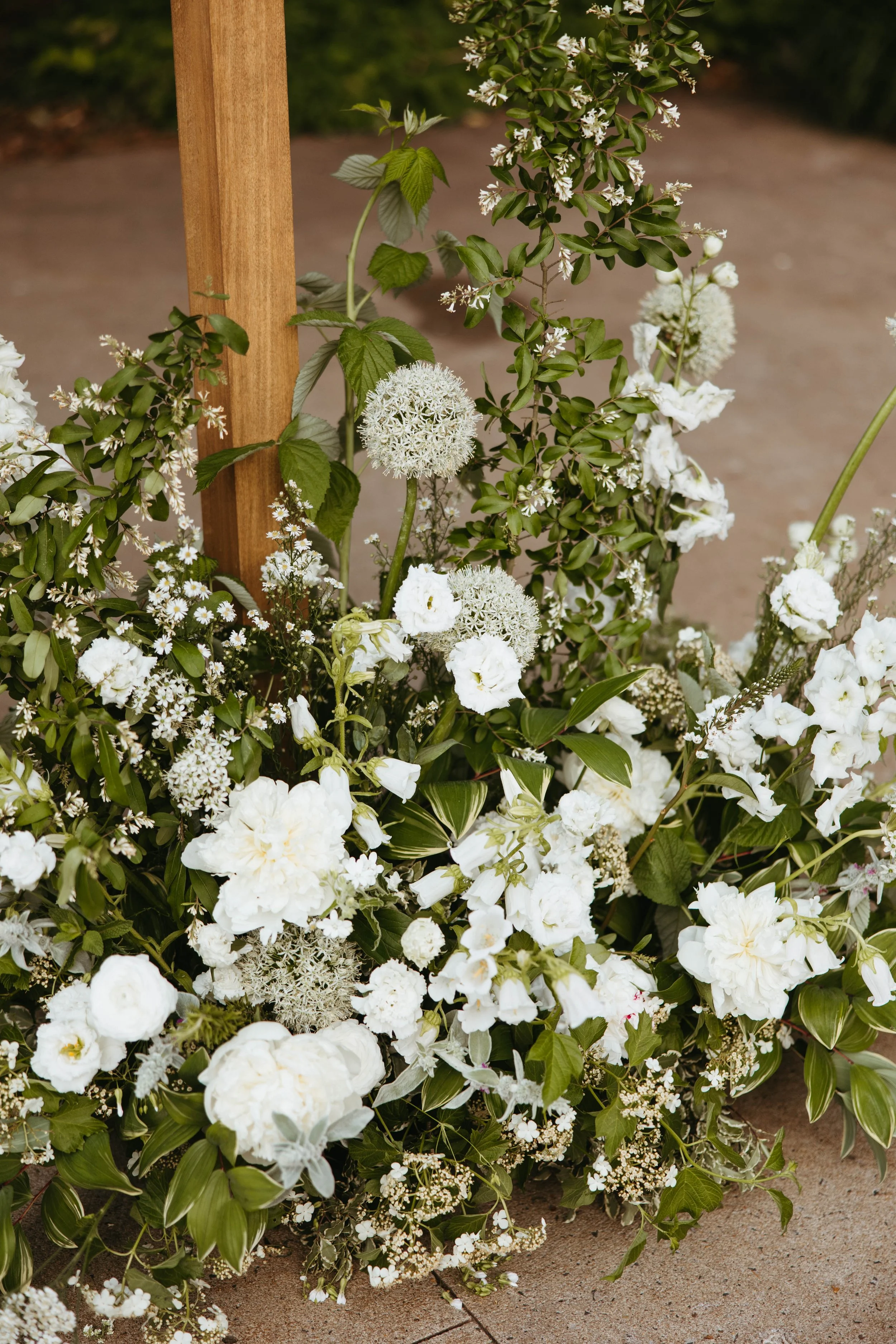 White floral arrangement with various flowers and greenery in front of a wooden post.