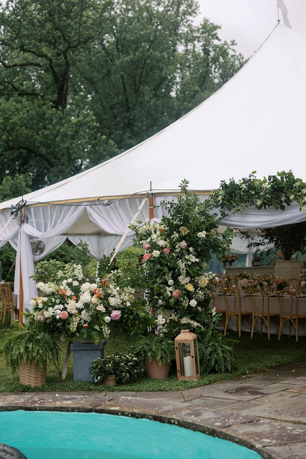 A decorated outdoor event tent with floral arrangements and lanterns near a pool.