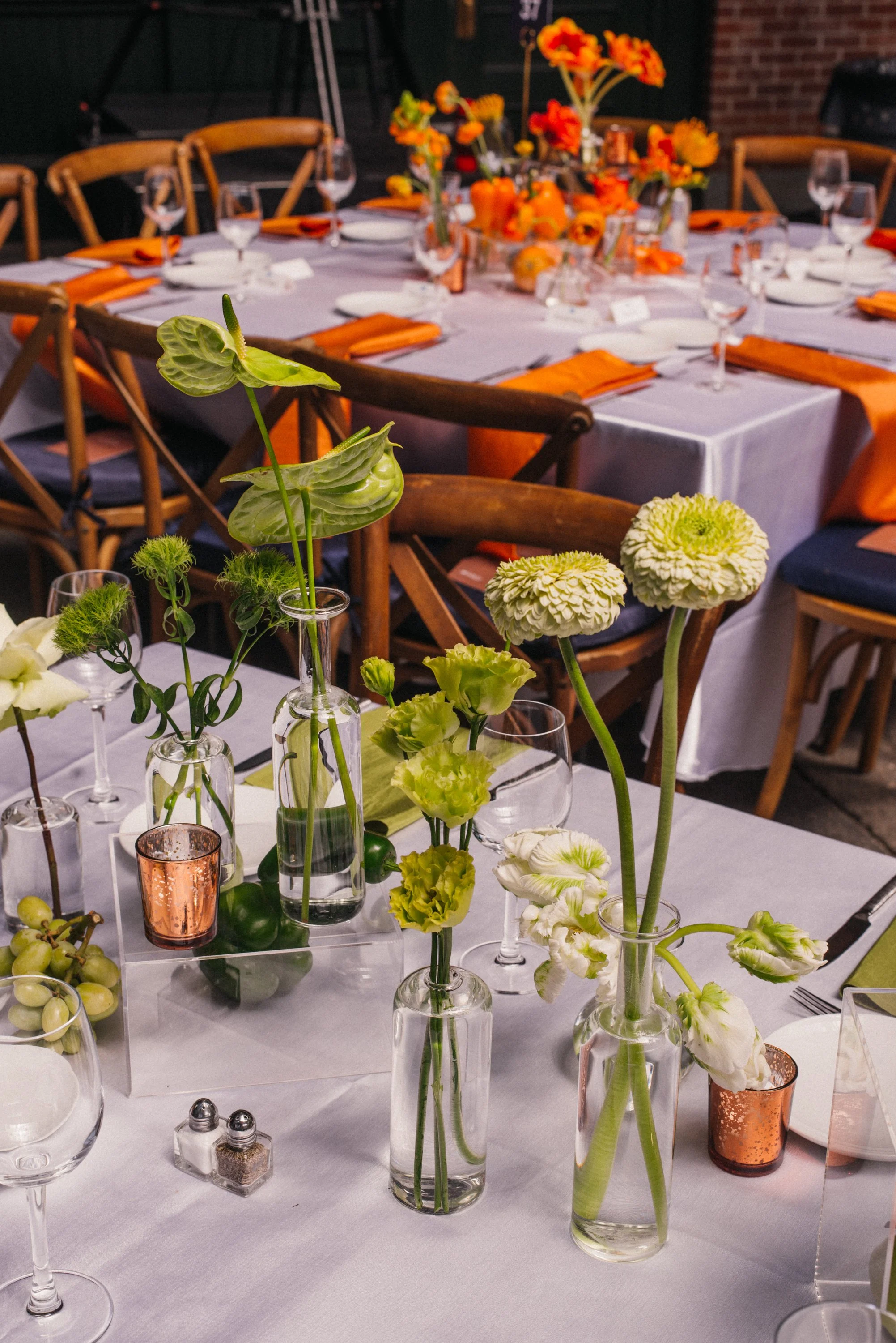 A banquet table set with white tablecloths, orange napkins, and glassware, decorated with orange and yellow flowers in vases
