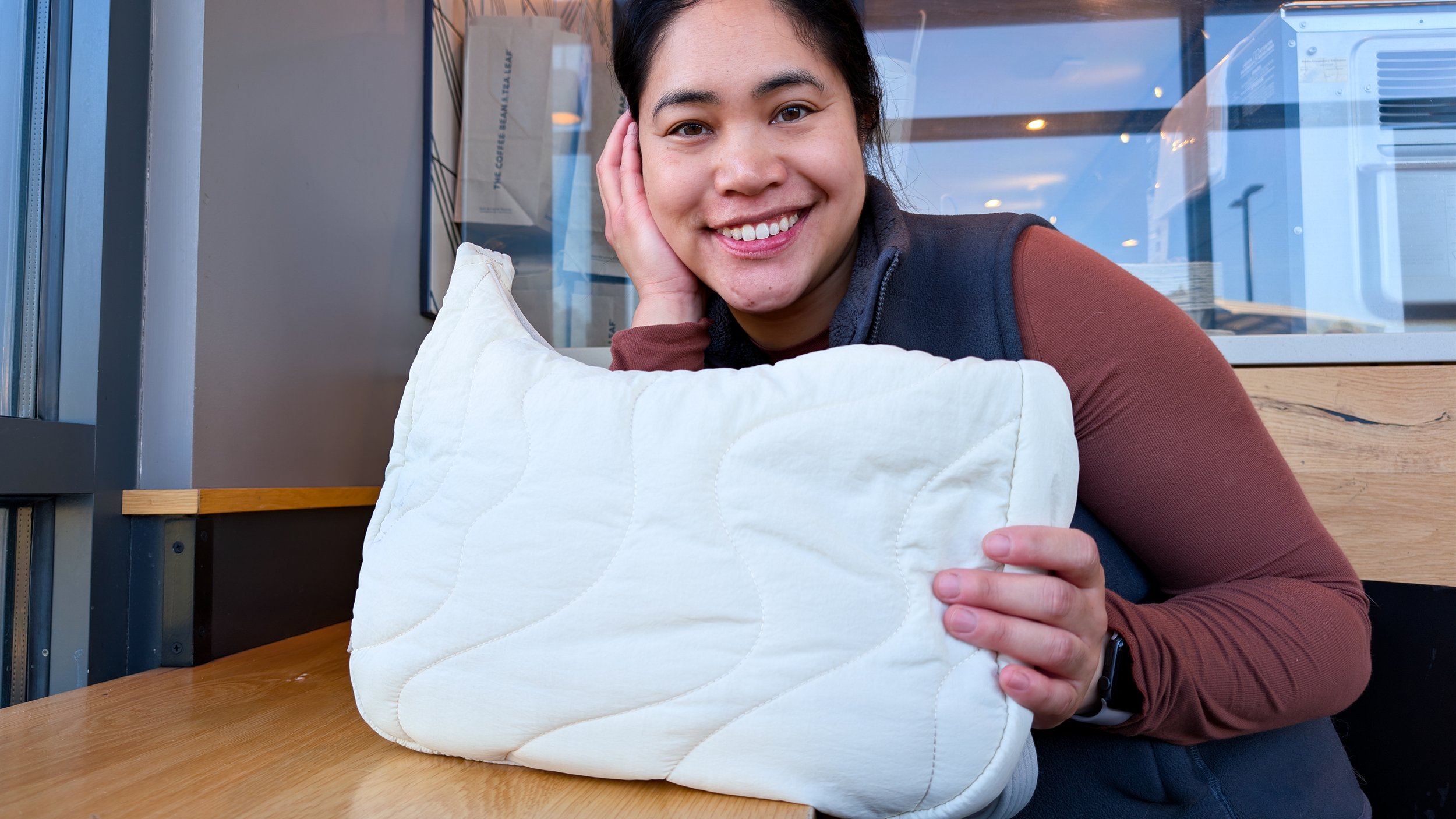 Girl smiling at camera next to Tomtoc 9L puffer crossbody bag in a review by The Sypnotix