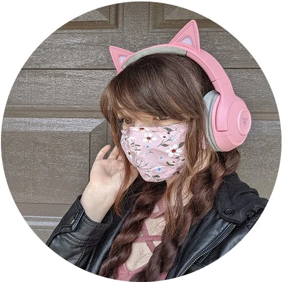 A young woman with dark brown hair in a mask and pink headphones
