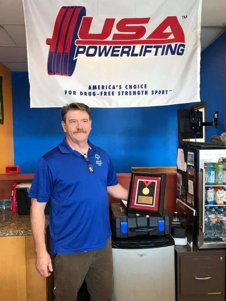 Hal Loyd, prior owner of Southside Strength and Fitness, holding a USA Powerlifting award inside the gym.