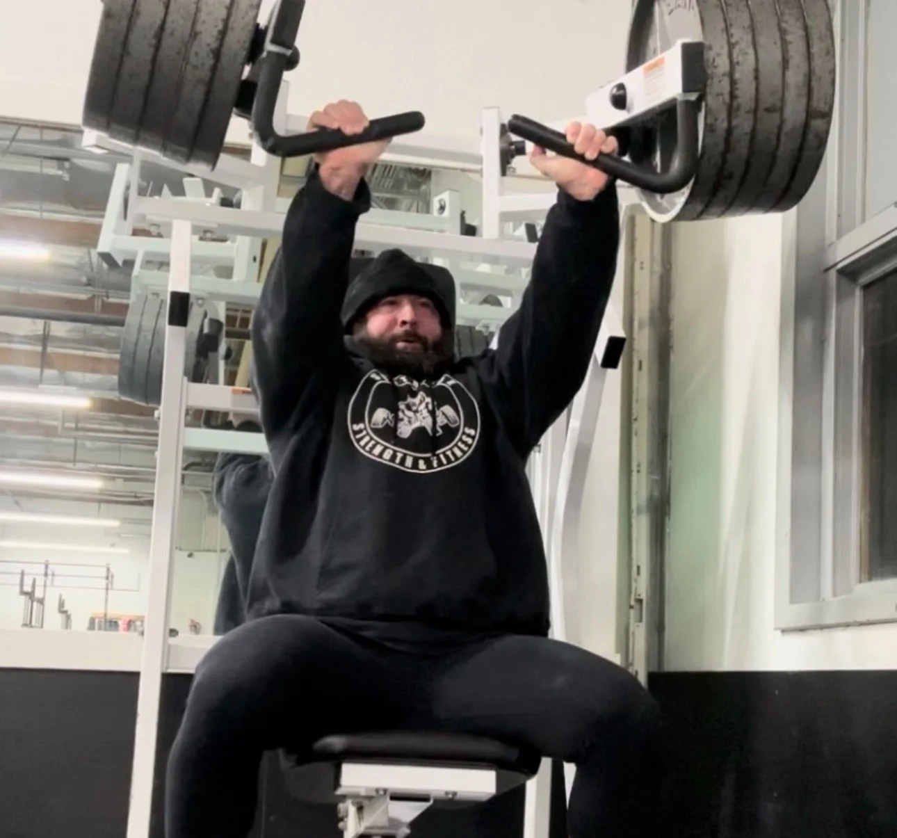 Southside member Wayne training with heavy weight plates, performing a seated overhead press using top-tier gym equipment.