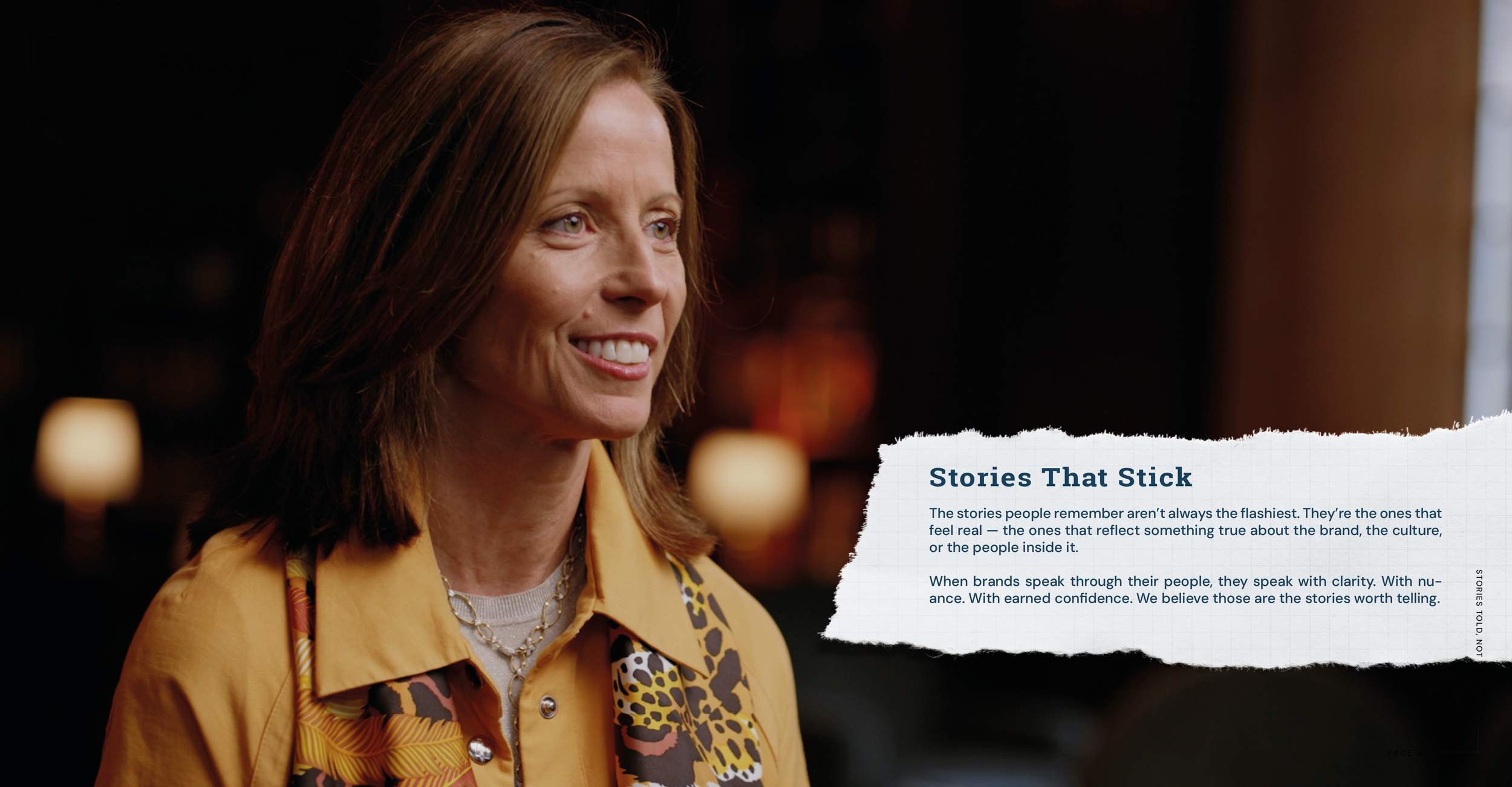 A woman with shoulder-length auburn hair wearing a yellow shirt, a leopard-print scarf, and a silver necklace, smiling in a warmly lit indoor setting.