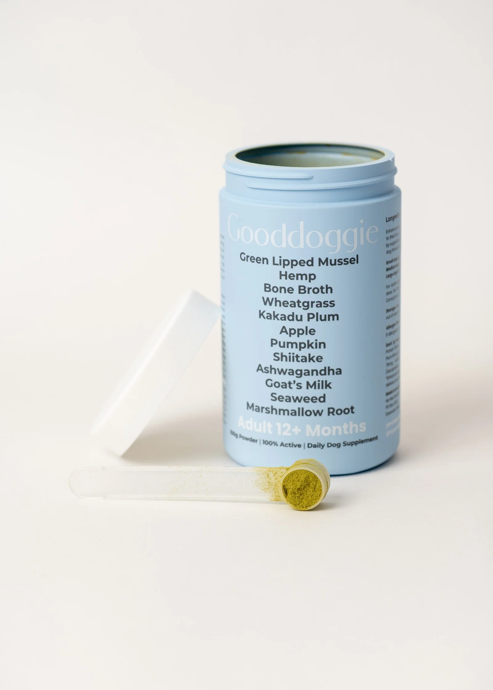 A blue container labeled 'Gooddoggie' with a list of ingredients for a dog supplement, and a small transparent tube with green powder.
