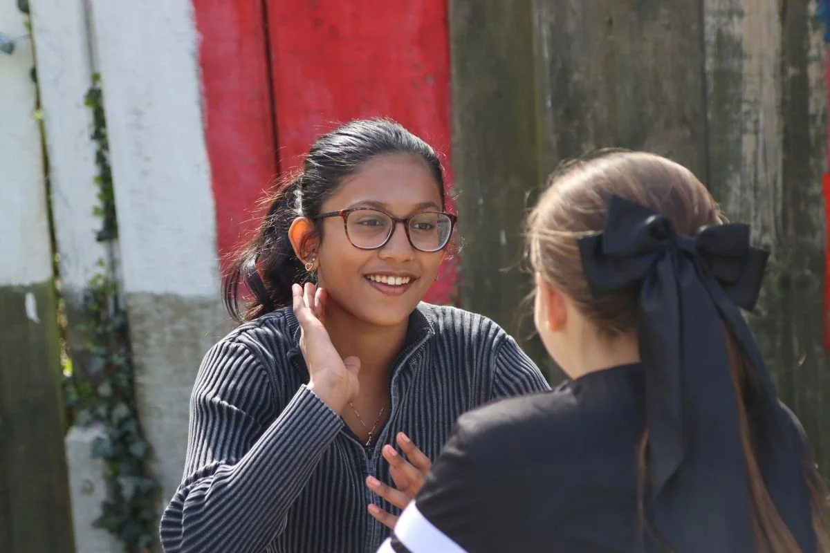 Two teenage girls sat at a picnic bench outside chatting and smiling