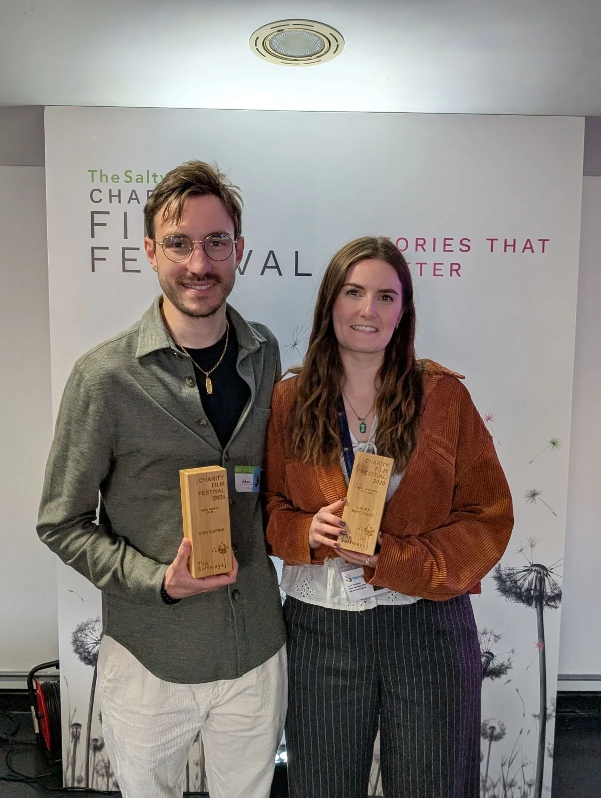 Man and woman stand next to each other holding Saltways Charity Film Festival awards won by children's mental health charity, Kids Inspire