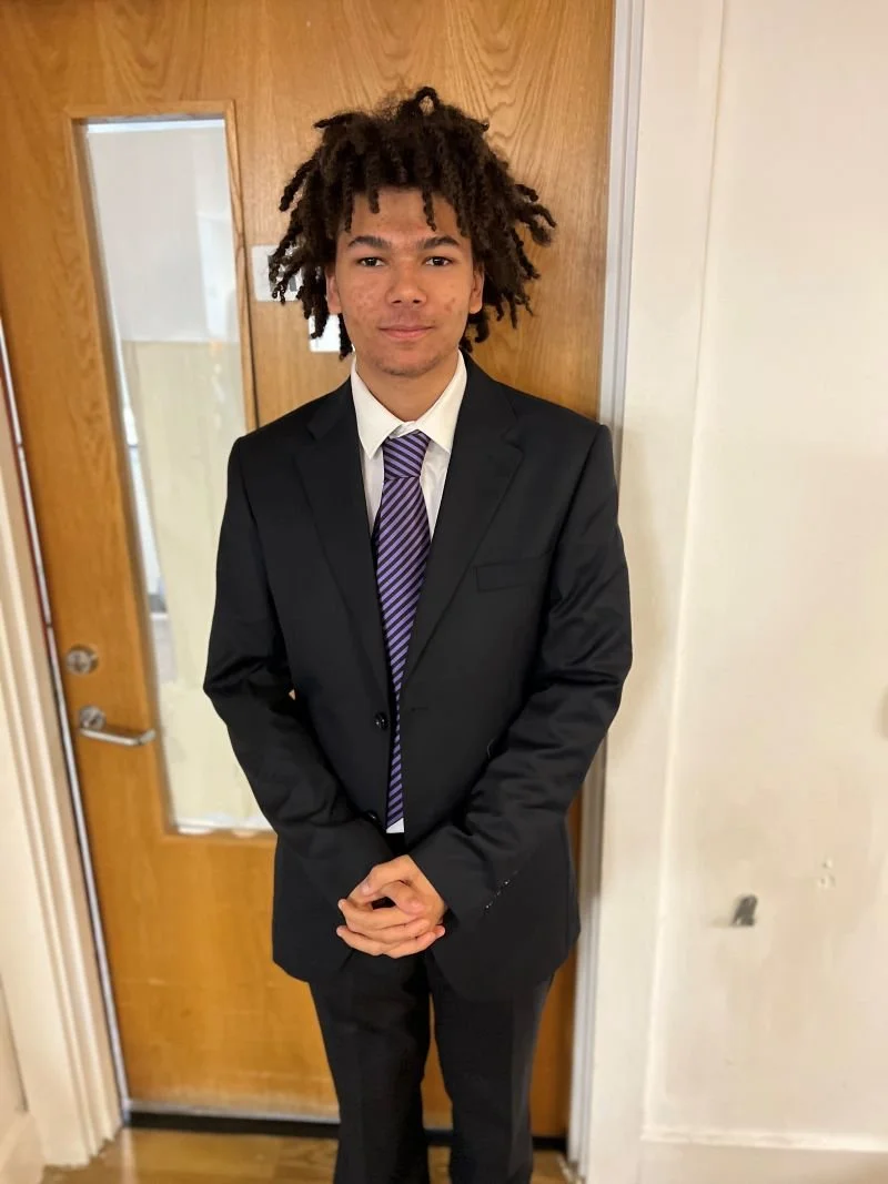 Teenage boy with dreadlocked hair wearing a black suit, white shirt and blue patterned tie at Kids Inspire's PROM-Unity event.