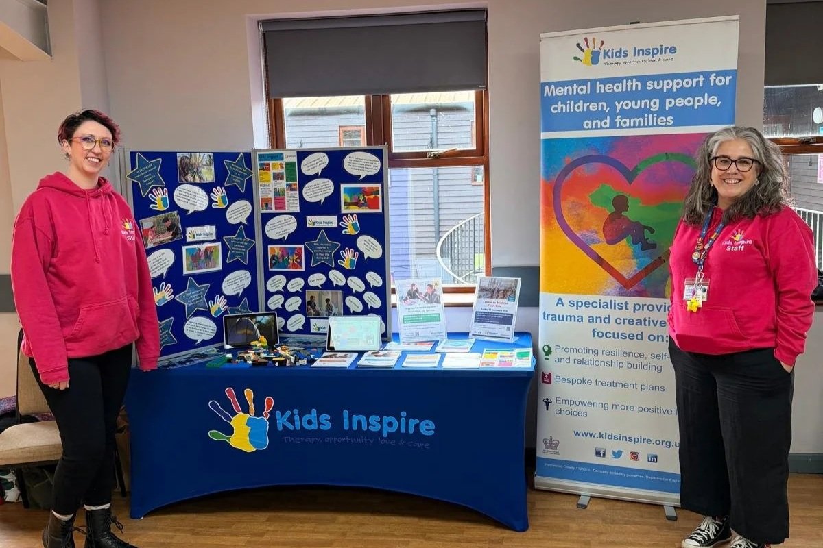 Two Kids Inspire community engagement team smiling at an event by their branded stand.