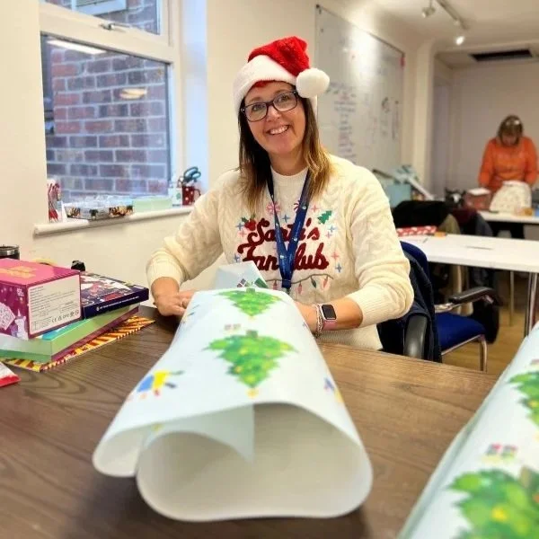 A Kids Inspire Christmas Appeal volunteer dressed in a Christmas hat wrapping children's gifts for our Christmas Appeal