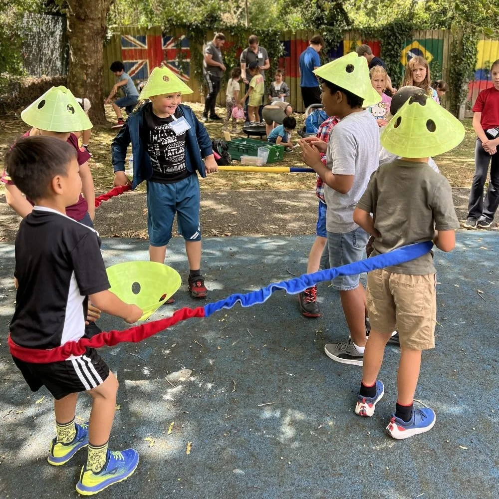 Children playing a team game outside with cones on their head. They are at a Kids Inspire Holiday Club.
