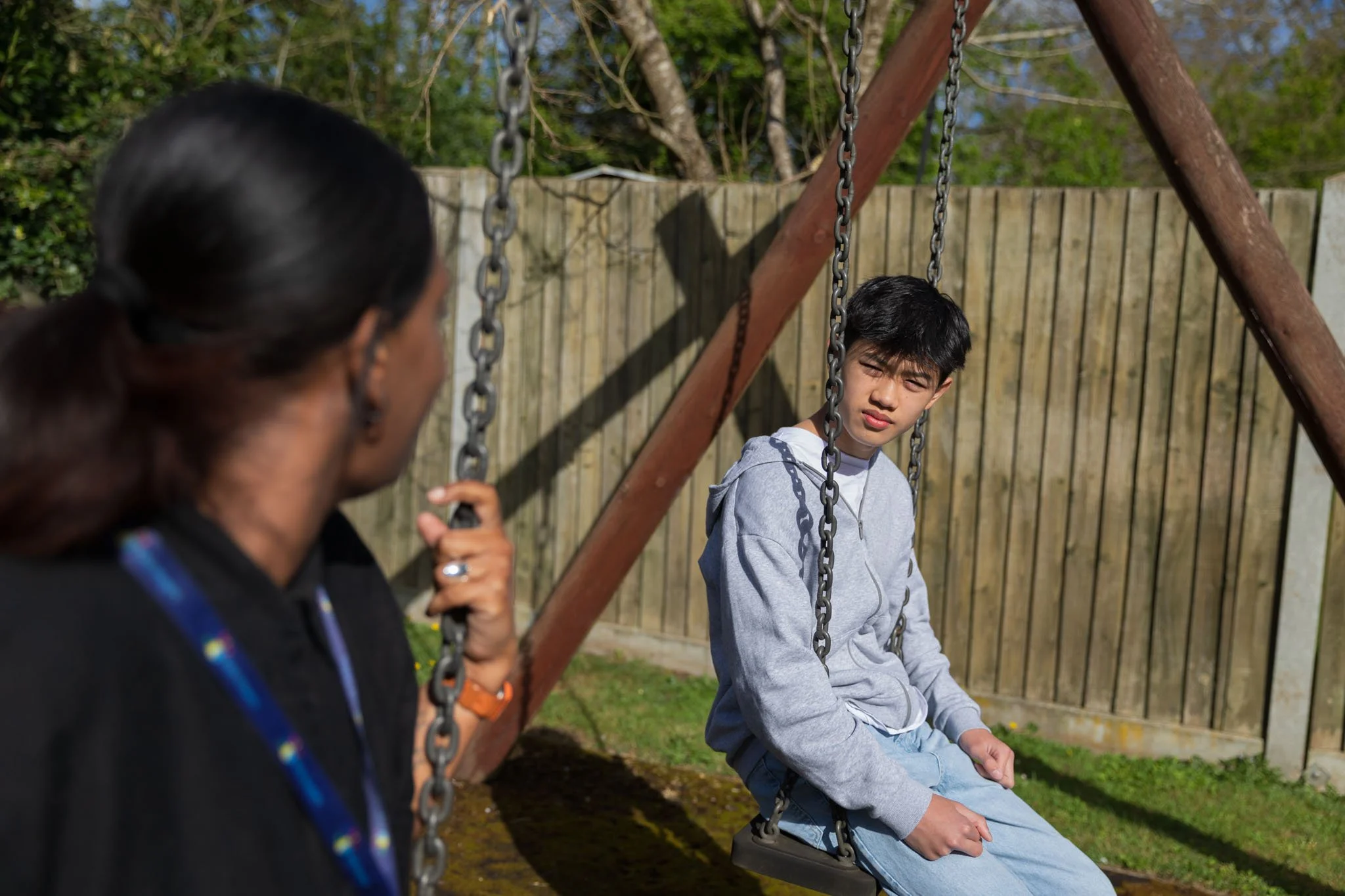 A Kids Inspire therapist sat on a swing next to a teenage boy while they engage in an outdoor therapy session