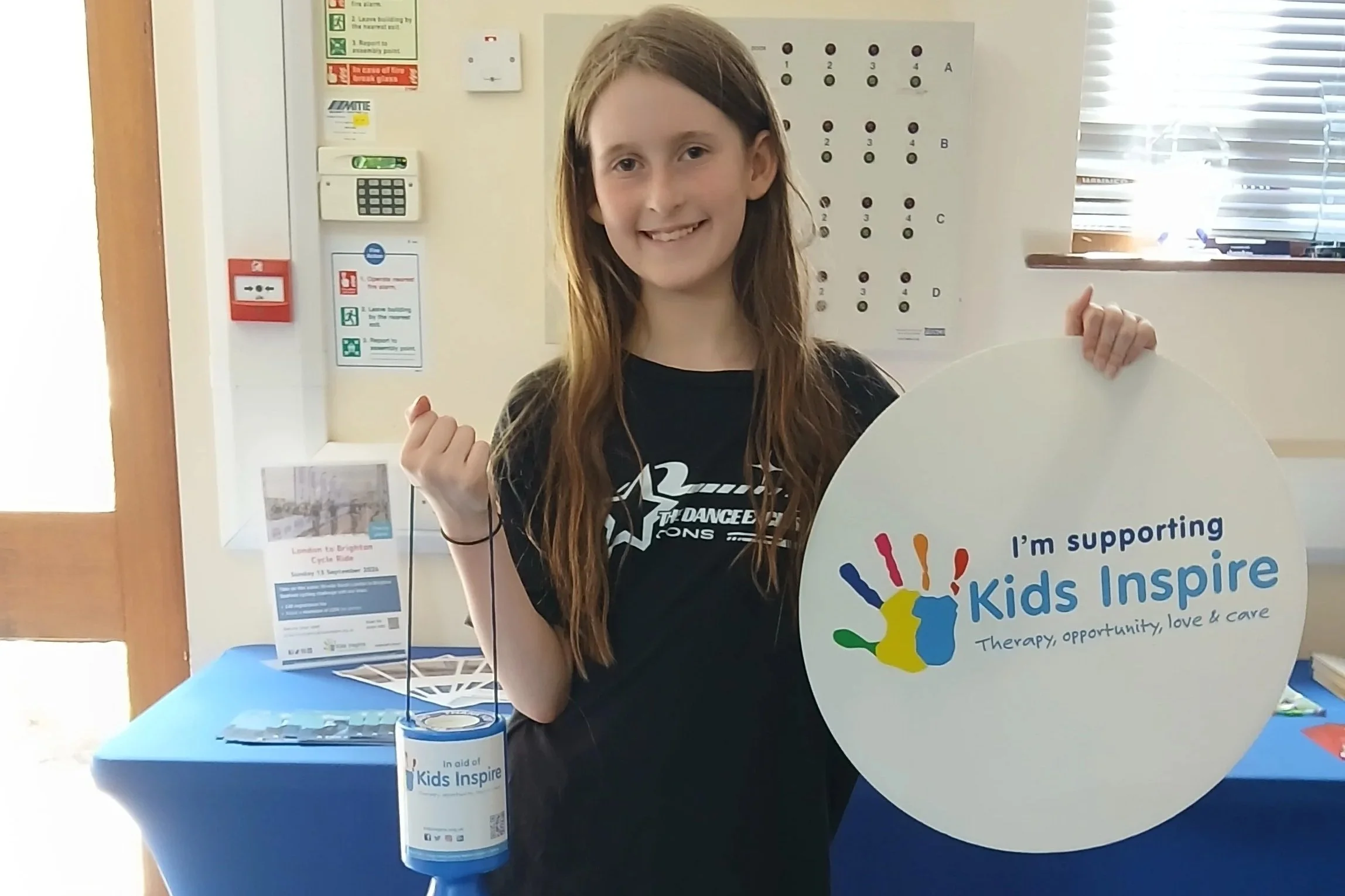 Child holding a Kids Inspire donation bucket and a sign that says I'm supporting Kids Inspire.