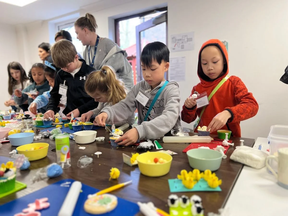 A group of children decorating cakes and biscuits with adults helping
