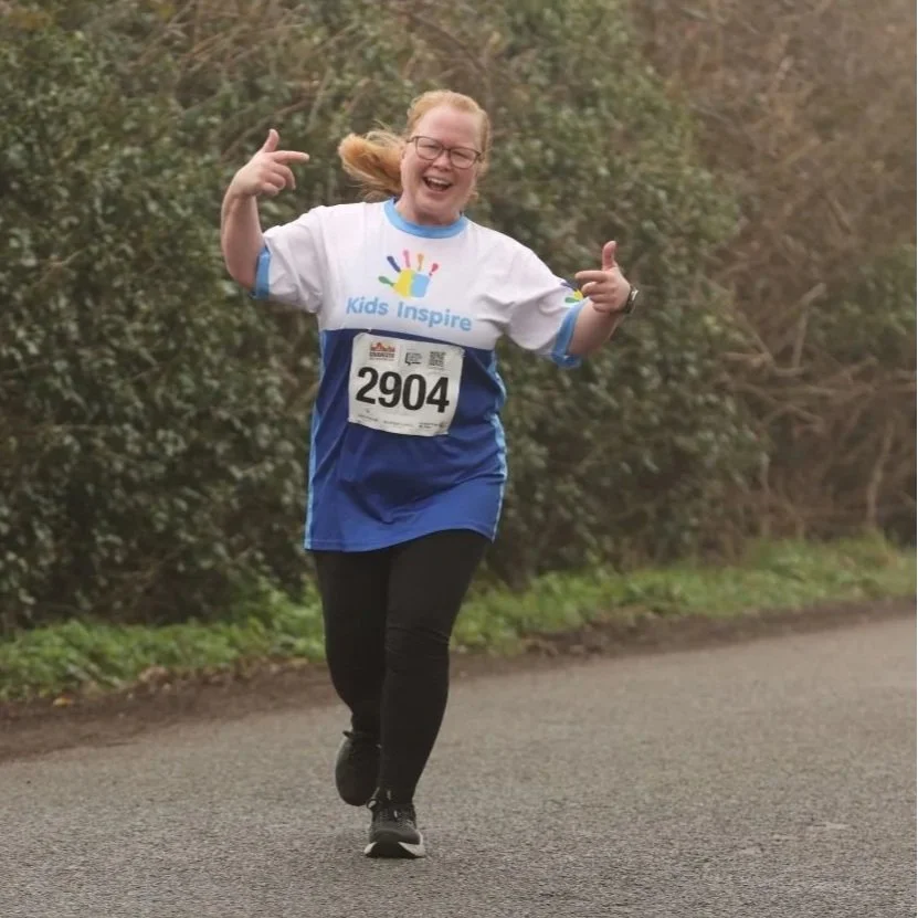 Runner wearing a Kids Inspire branded running top, and celebrating as they near the finish line.