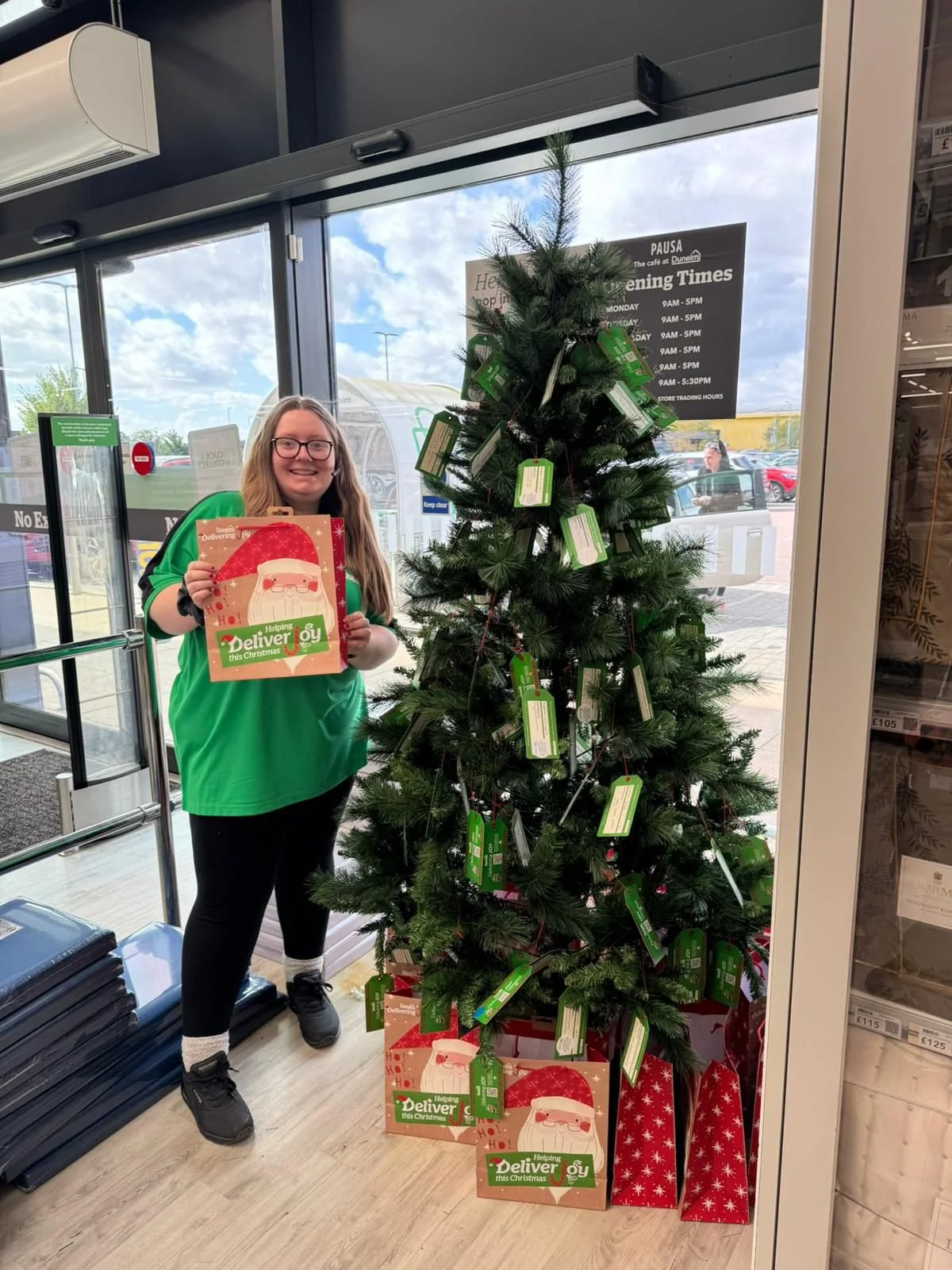 Chelmsford Dunelm staff member holding up a Delivering Joy Christmas gift bag as part of Kids Inspire's Christmas Appeal.