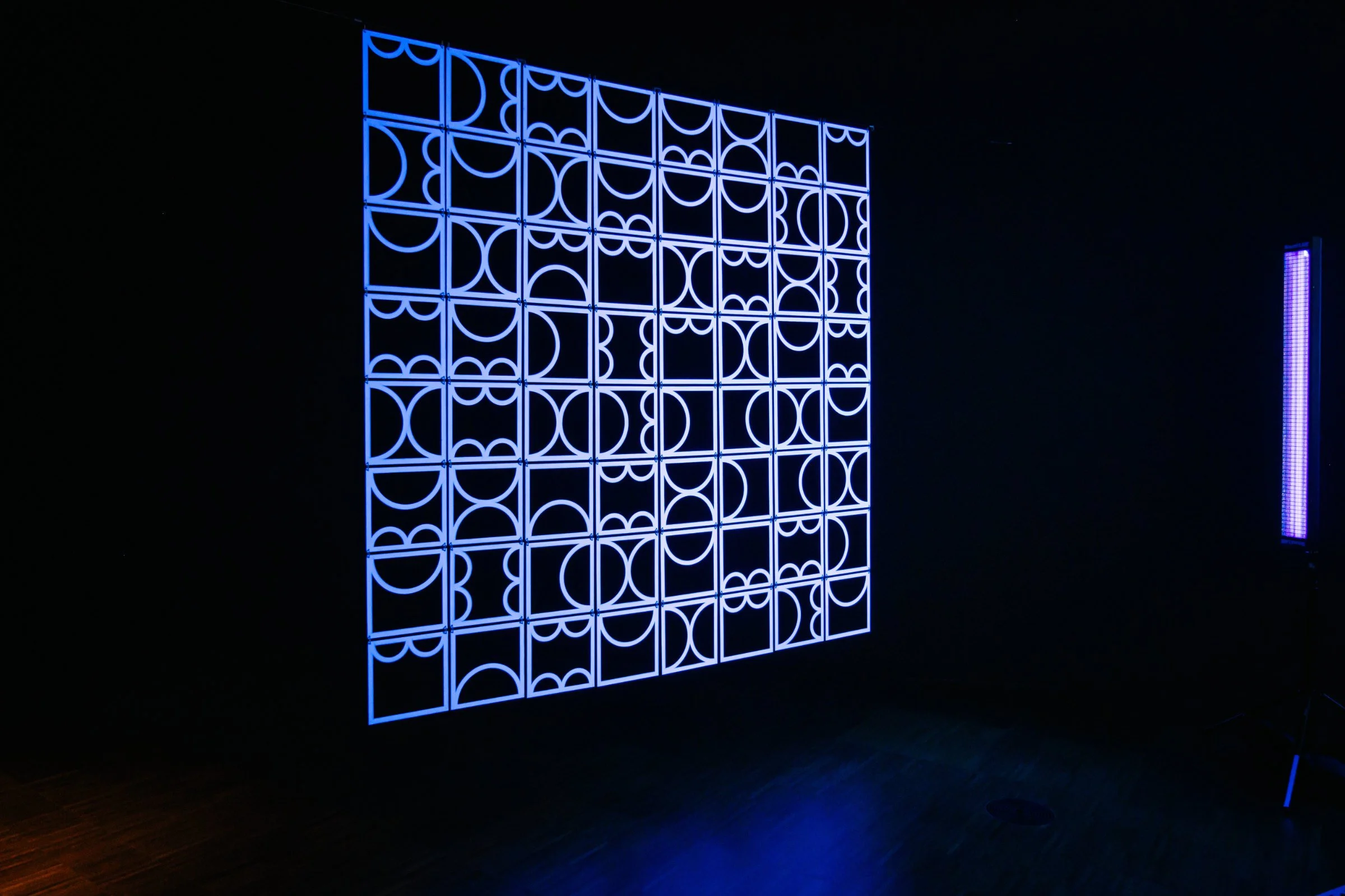 Side view of shemza.digital #9 showing the suspended geometric structure and ultraviolet light used to illuminate the fluorescent painted surfaces.