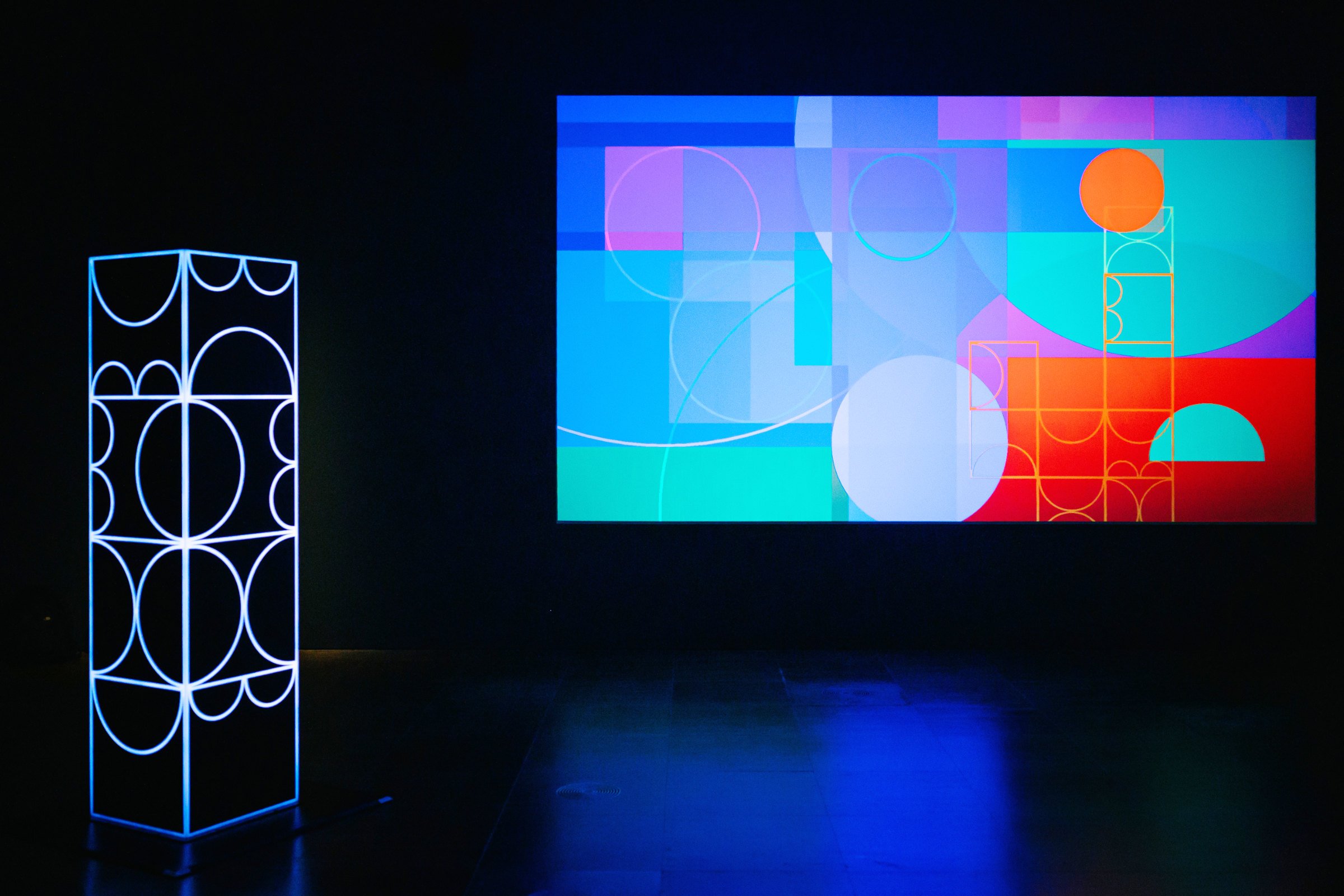 Gallery installation view of shemza.digital #6, an interactive light sculpture displayed alongside a projected digital artwork.