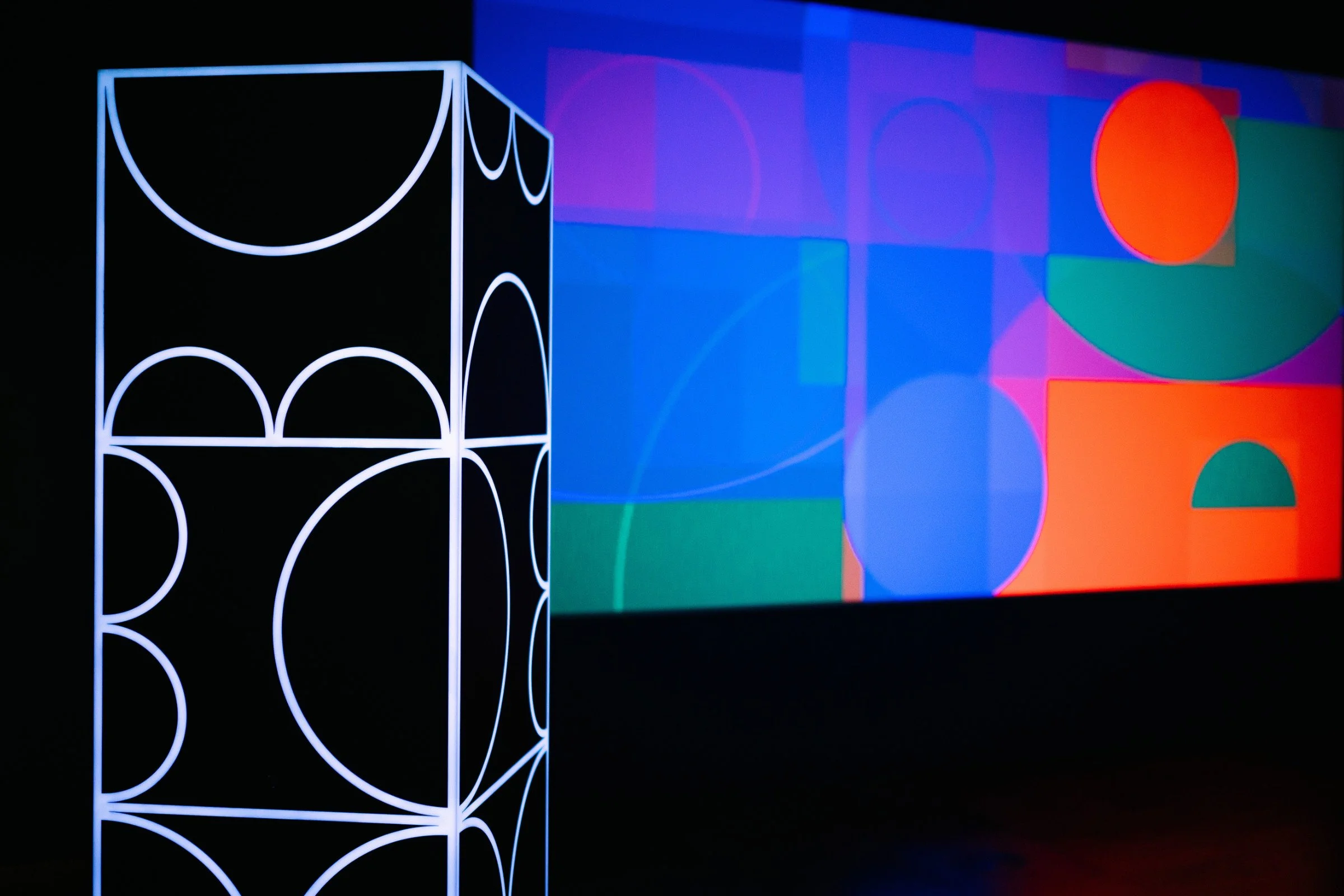 Detail of shemza.digital #6, showing the illuminated acrylic sculpture with a digital projection in the background.