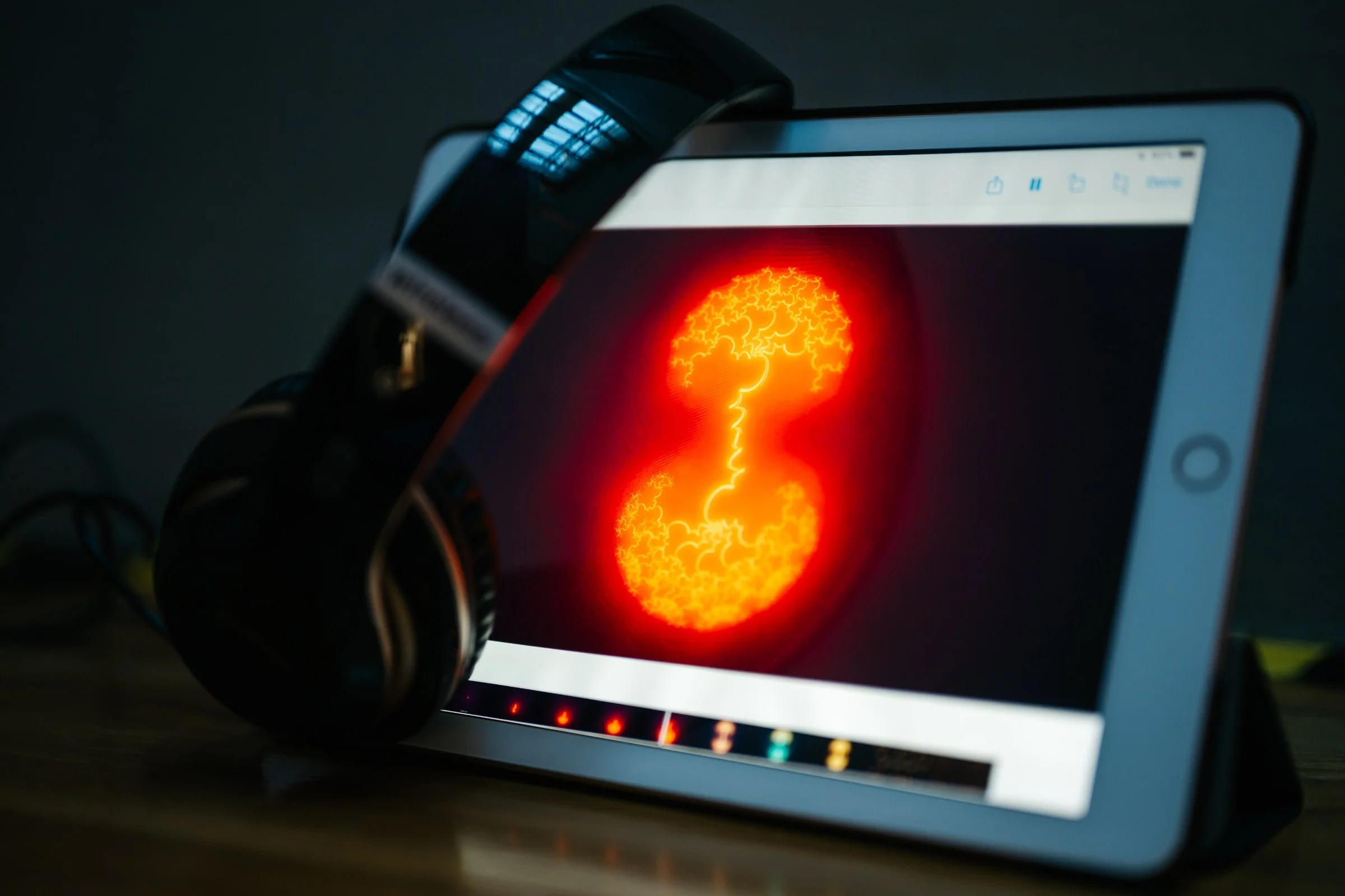 Close-up of shemza.digital roots #1 displayed on an iPad with headphones, showing glowing red calligraphic forms from the audiovisual meditation artwork.
