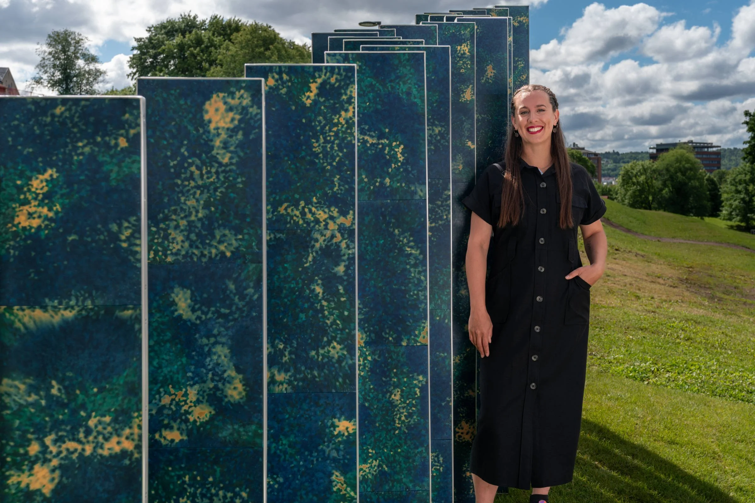 Artist Aphra Shemza standing beside the wave-shaped Ocean Rise sculpture in Tøyen Park, Oslo.