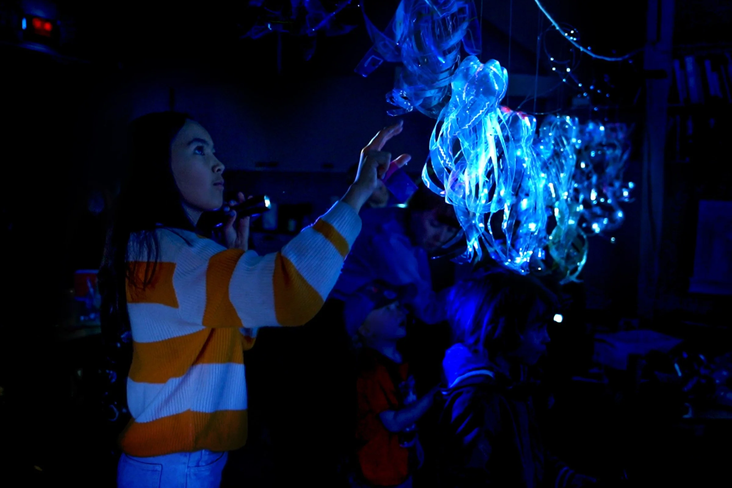Children illuminating their recycled-plastic jellyfish to create a glowing underwater diorama during the Ocean Rise workshop.