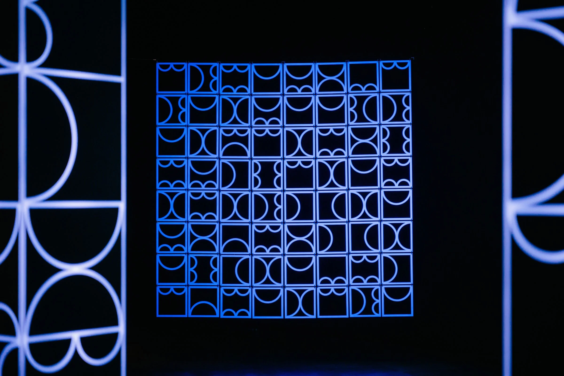 Full view of shemza.digital #9, a large-scale hanging geometric sculpture created from UV-painted panels and illuminated with ultraviolet light.