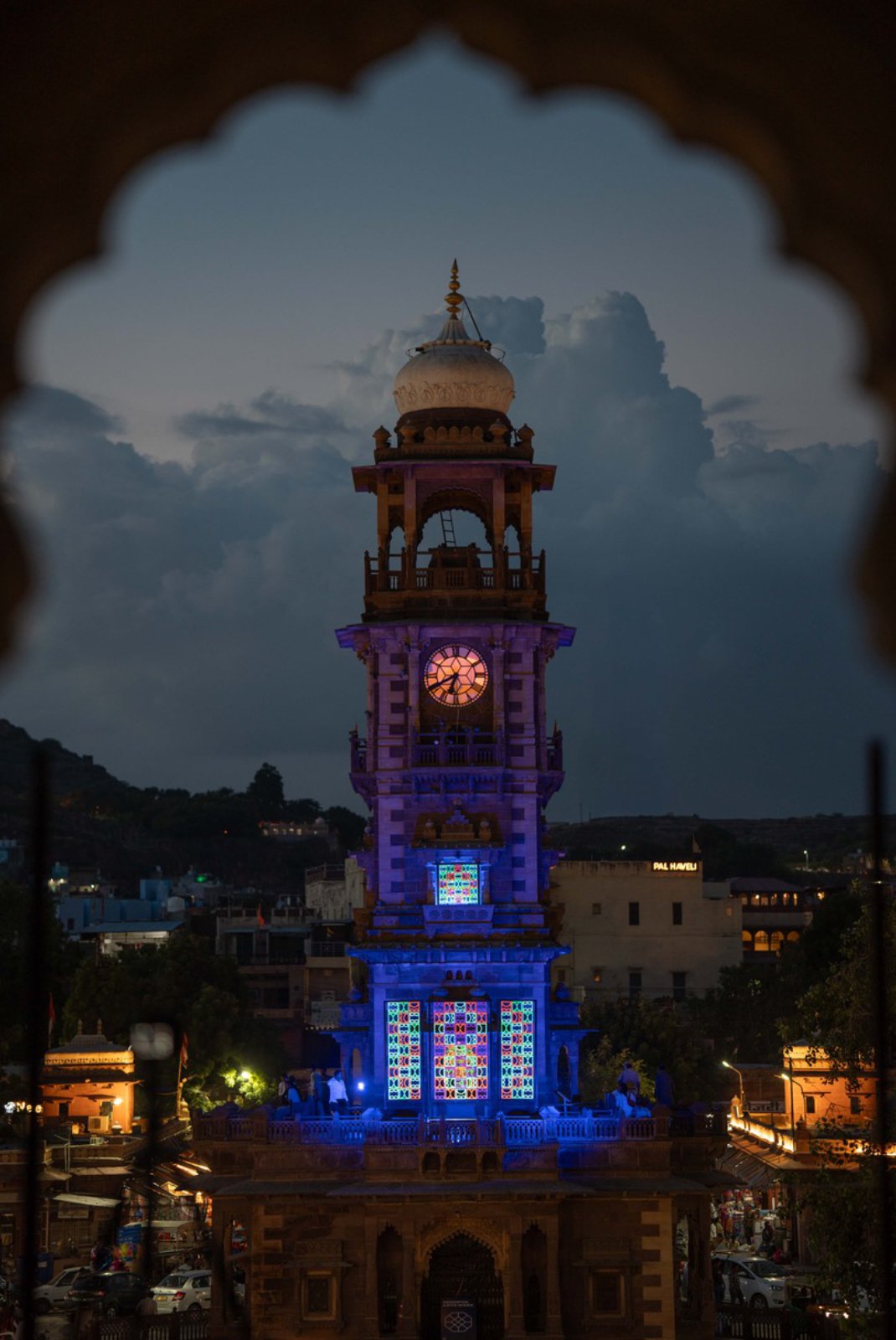 View of shemza.digital #17 framed by an ornate archway with the Clock Tower and Sardar Market in Jodhpur, India.