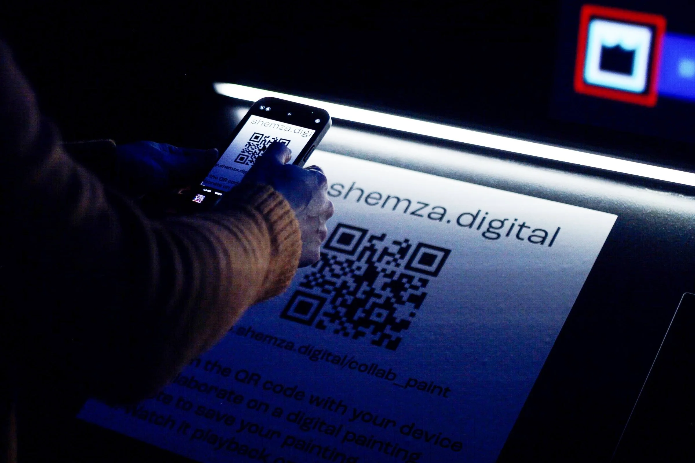Visitor scanning a QR code on their mobile phone to create a collaborative digital painting for shemza.digital #4–7.