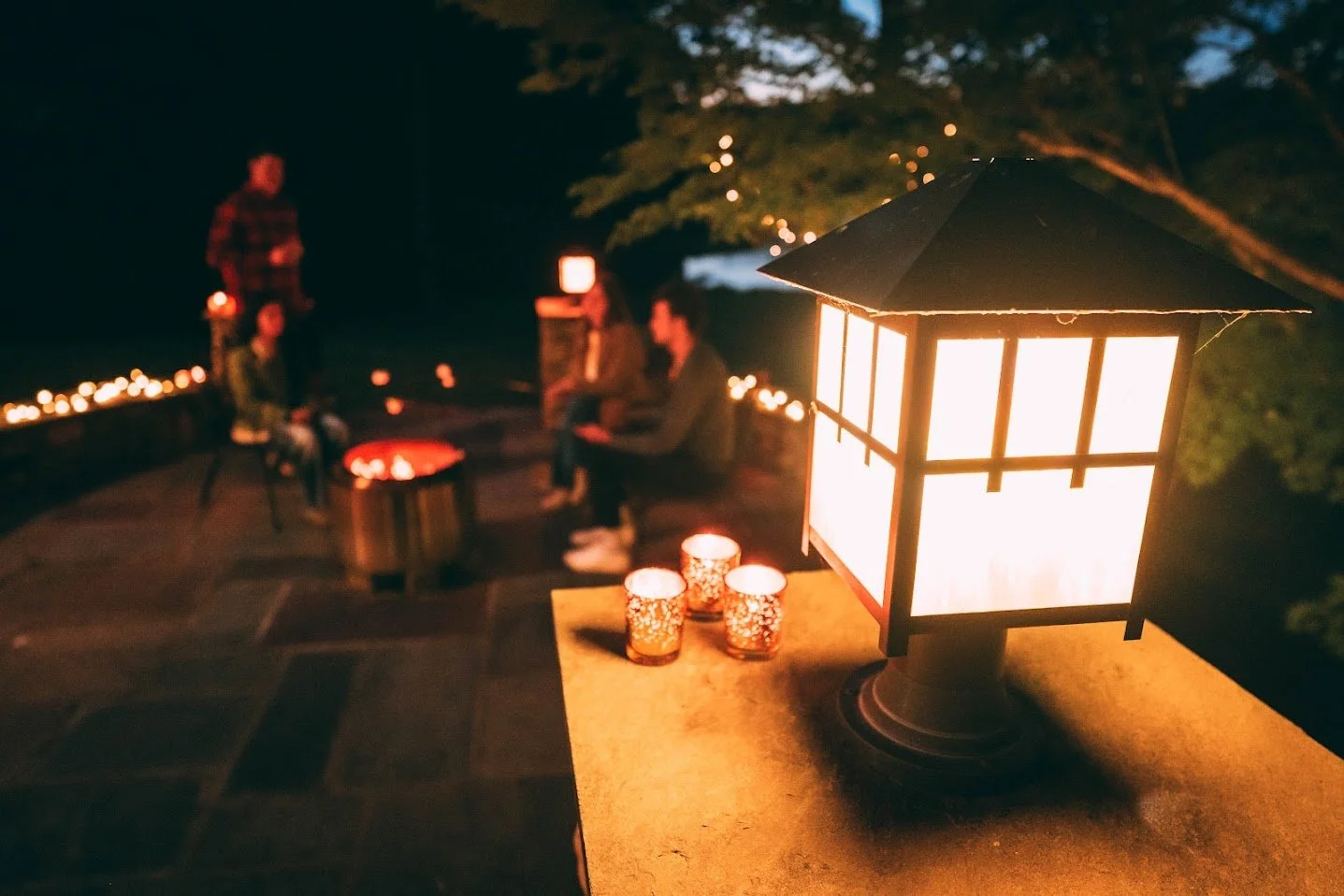 Evening holiday gathering at Southern C's Farm with flowing lanterns, candles, and guests enjoying a festive fireside and lakeside atmosphere