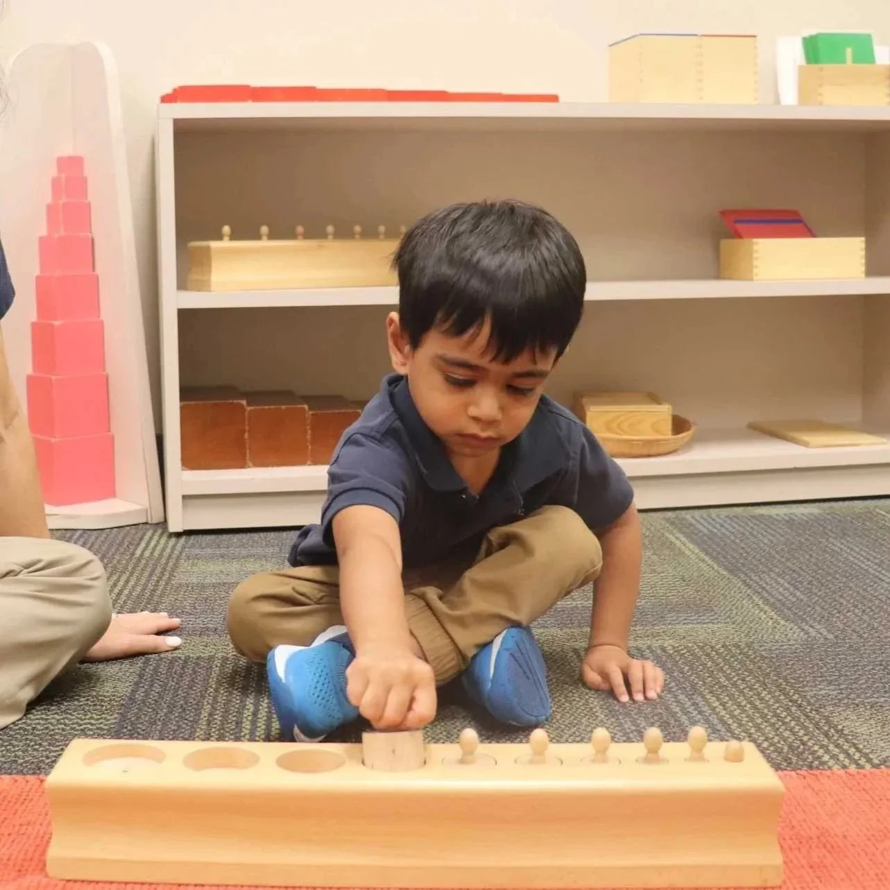 A Montessori student plays with cylinder blocks on the floor in an Allen, TX, classroom.
