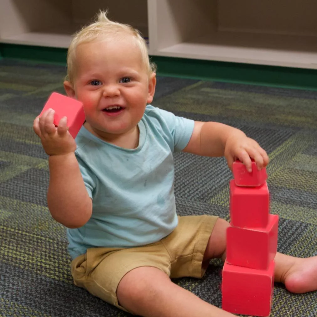 Infant stacking colorful Montessori blocks on a classroom floor in Allen, TX
