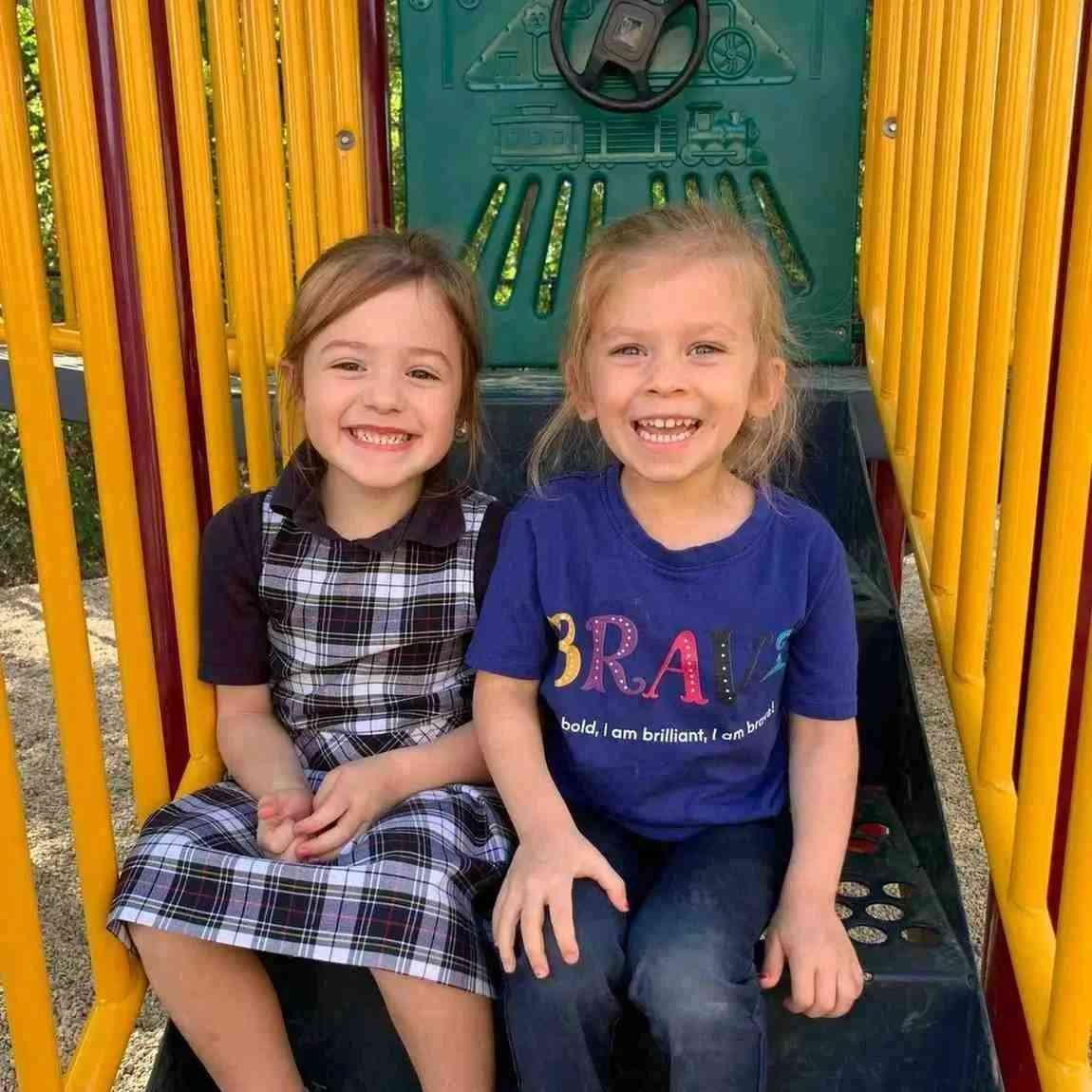 Two students sitting on a playground slide, enjoying outdoor preschool play in Allen, TX
