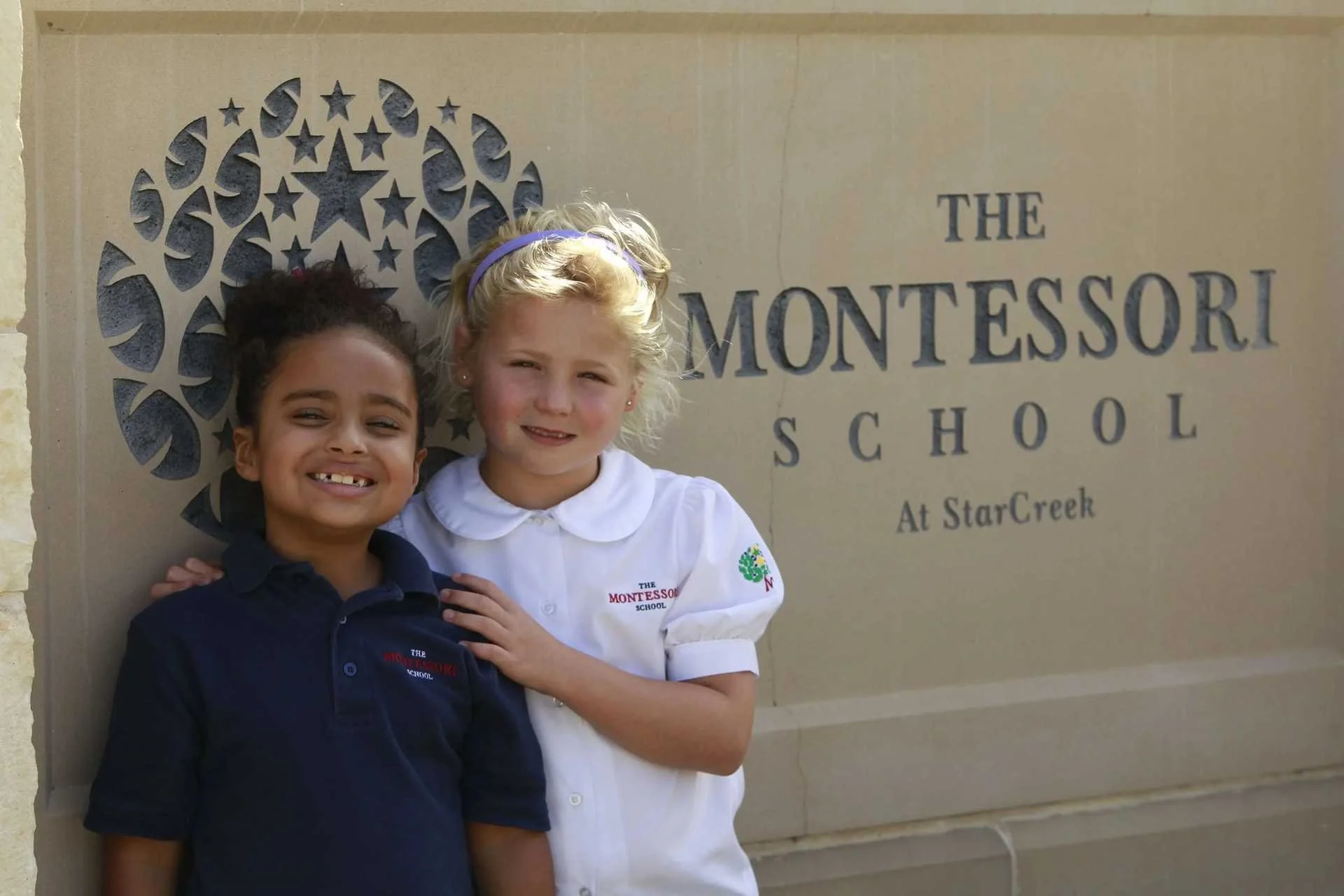 Two students standing in front of The Montessori school at the Starcreek signboard in Allen, TX
