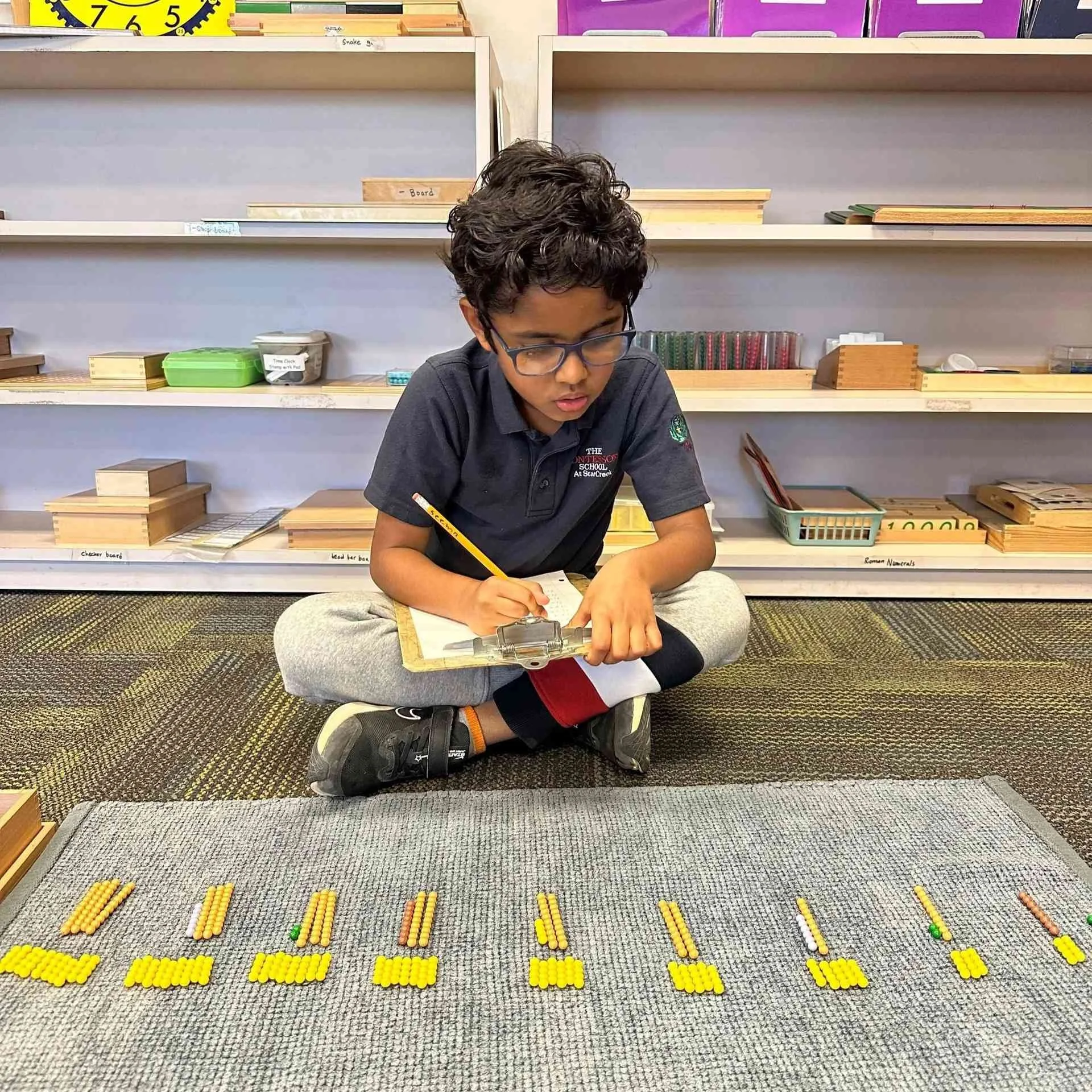 Student working with math materials and bead units while writing on a clipboard in Allen, TX
