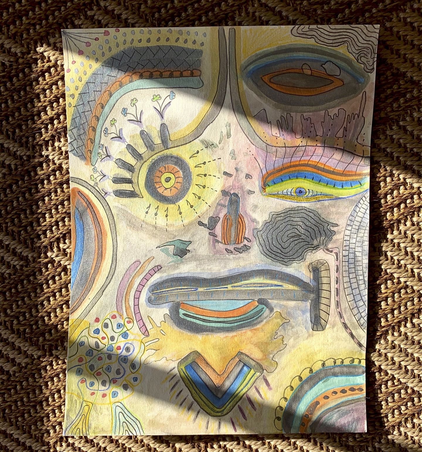 Colorful, abstract drawing with various shapes, lines, and symbols. Features include an eye with rainbow-colored lines, a central sun-like shape, and surrounding patterns and figures with vibrant, pastel, and dark colors.