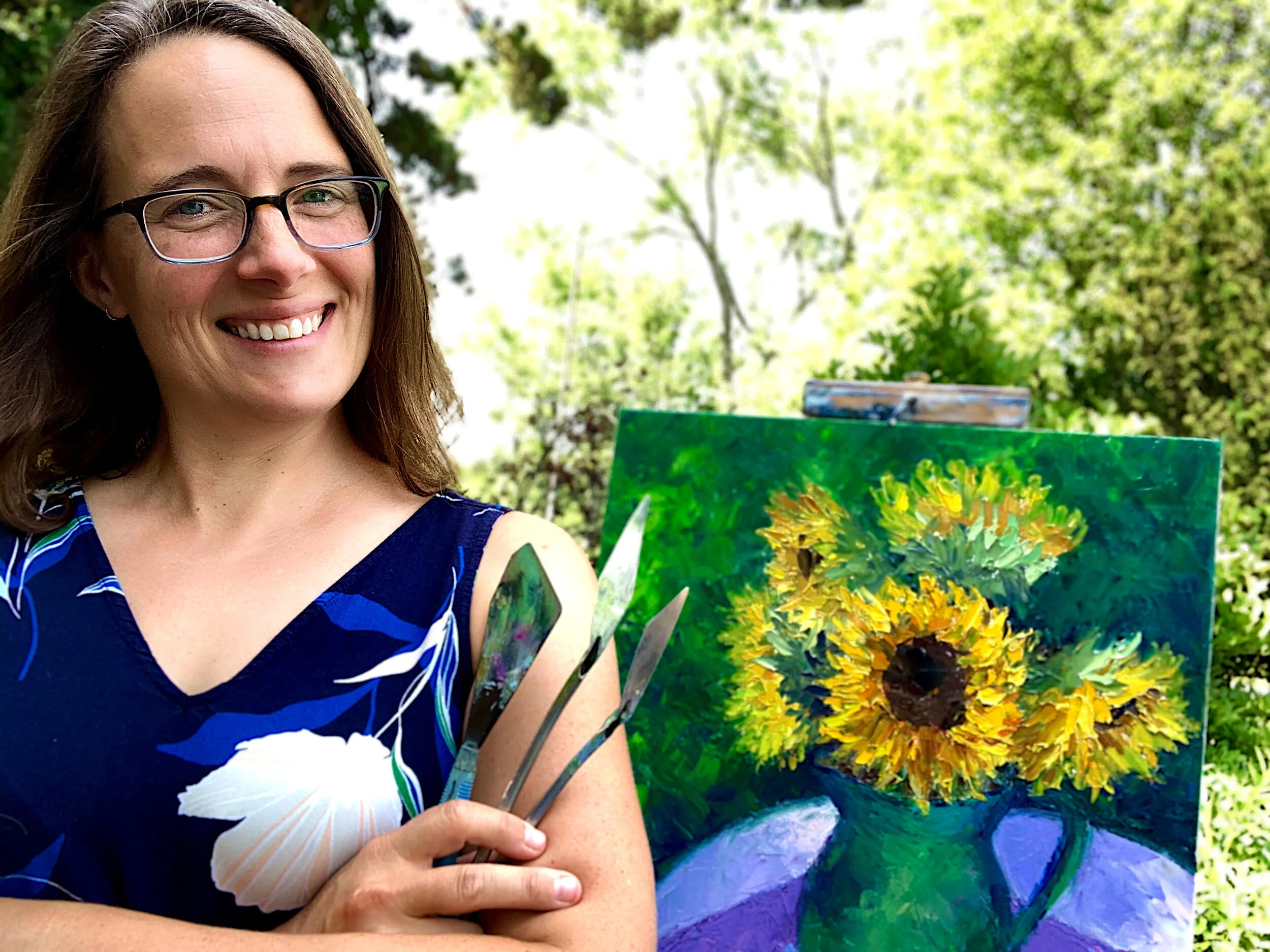 Artist, Maggie Capettini, smiling outside in front of her painting